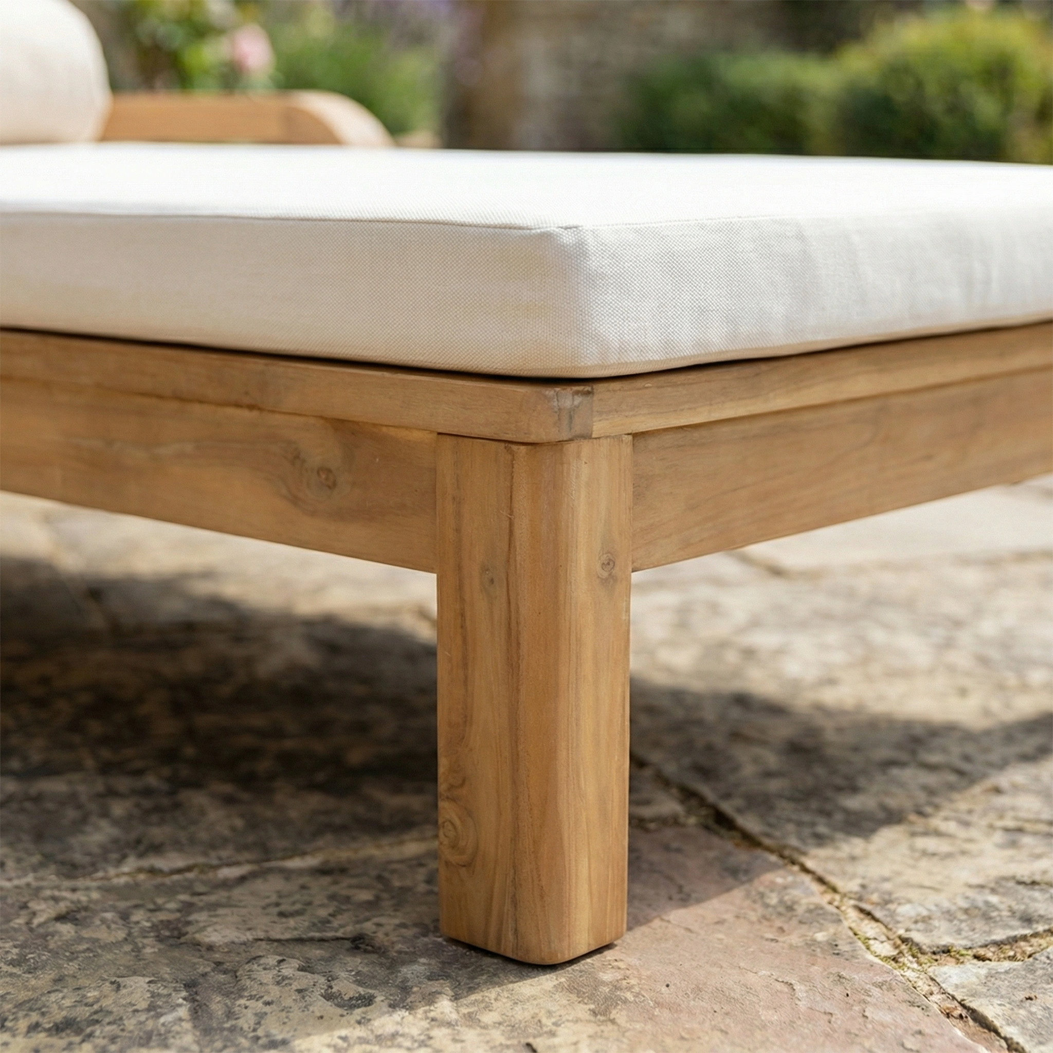 Close-up of the Quay Sun Lounger in Linen, highlighting its acacia wood leg and white cushion on a stone patio—an example of quality outdoor furniture.