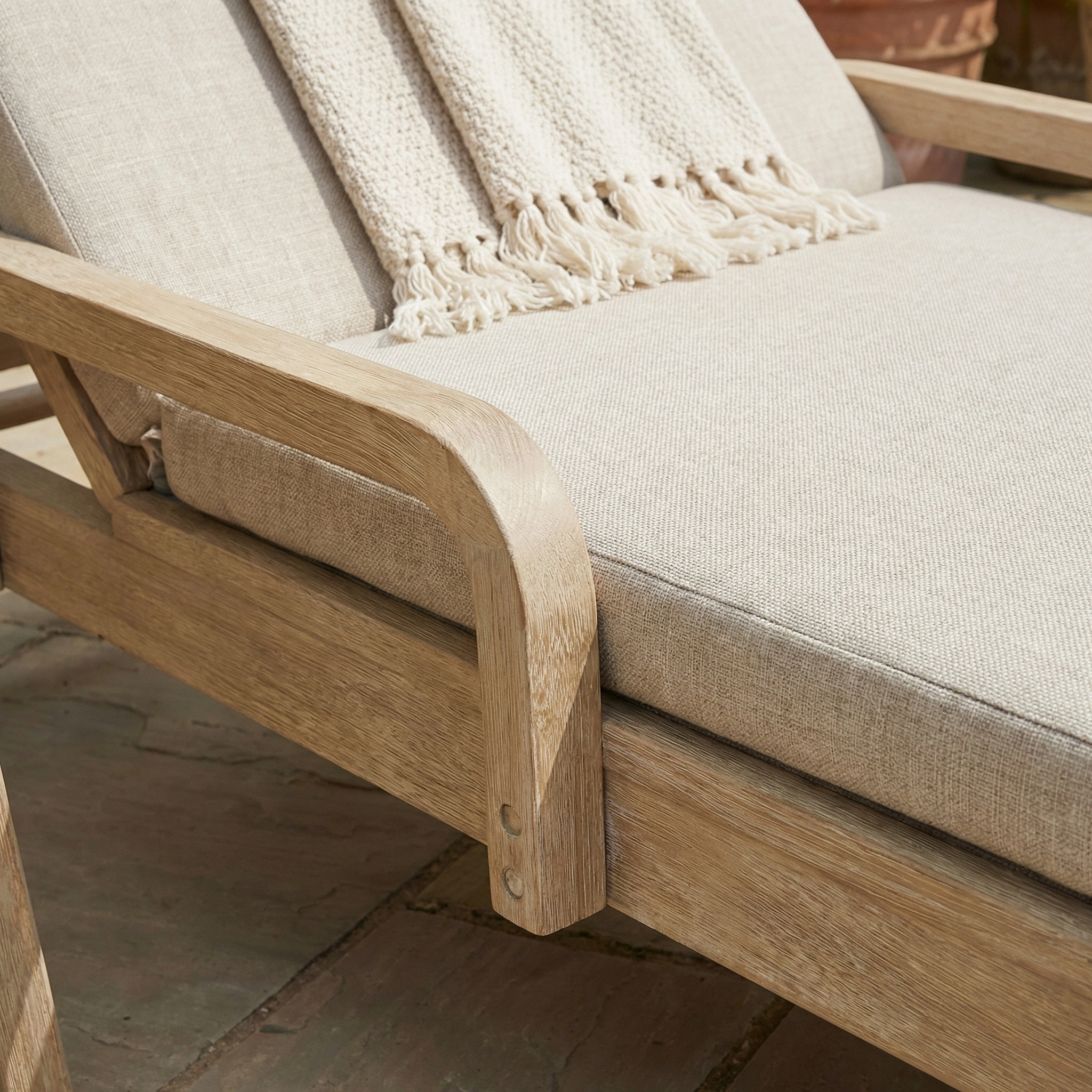 Close up of the Quay Sun Lounger in Mocha, a stylish garden furniture piece, with a textured throw blanket draped over it.