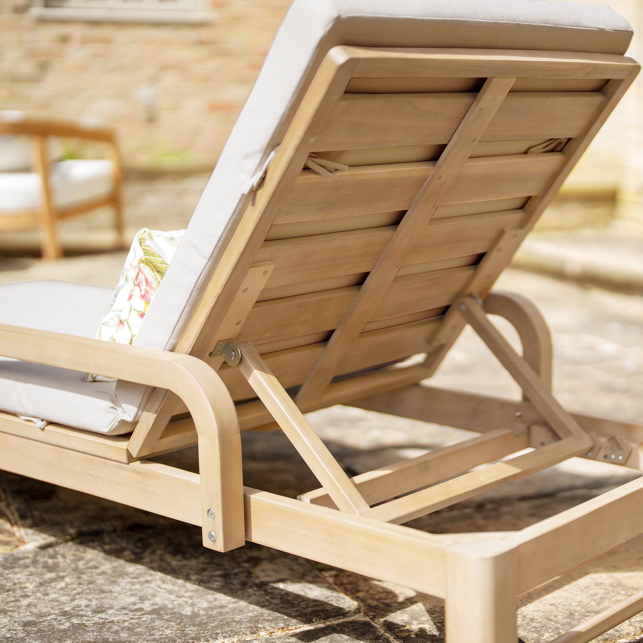 The Quay Sun Lounger in Mocha with light cushions, shown from the back at an angle on a stone patio—a stylish upgrade for any outdoor furniture setting.