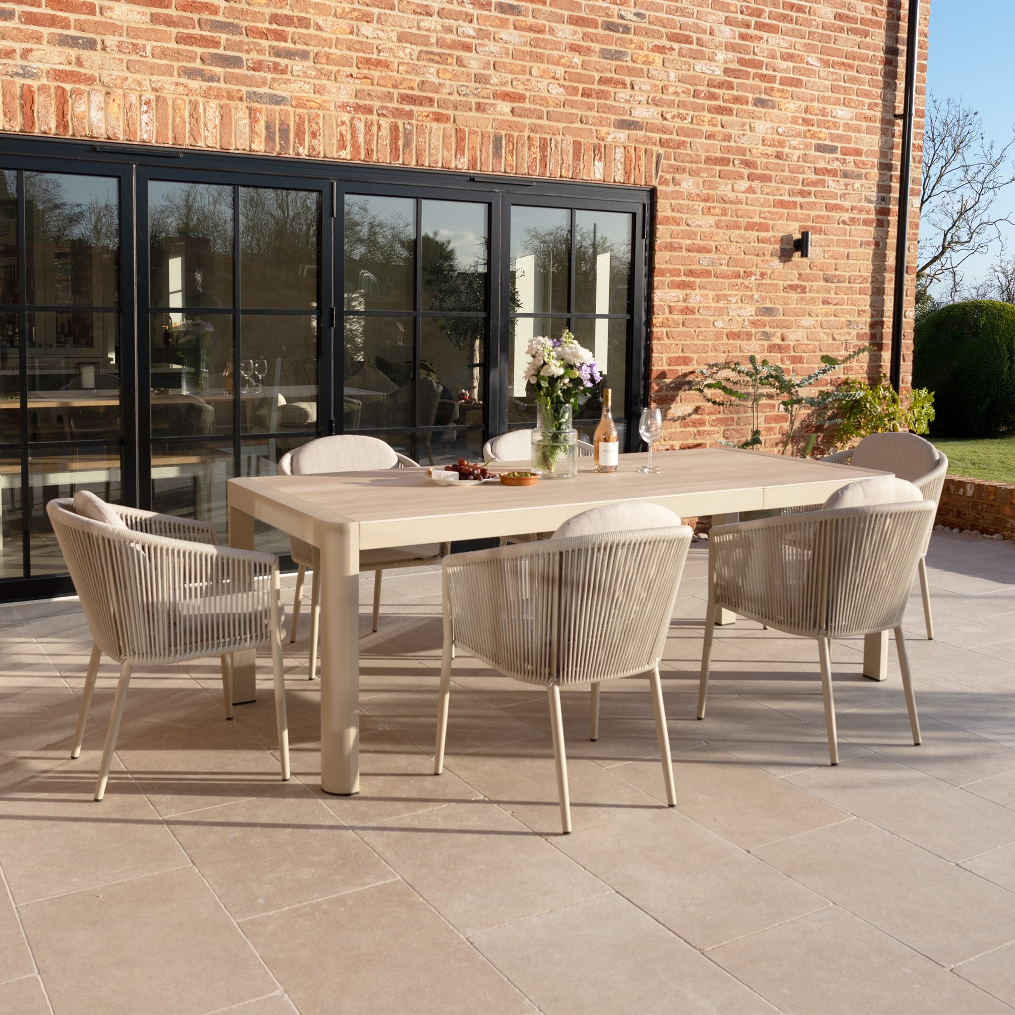 The Ravona 6 Seat Rope Extending Dining Set (162-222cm) in Latte features an aluminium frame and six chairs around a spacious table, making it ideal for stylish outdoor dining on your patio.