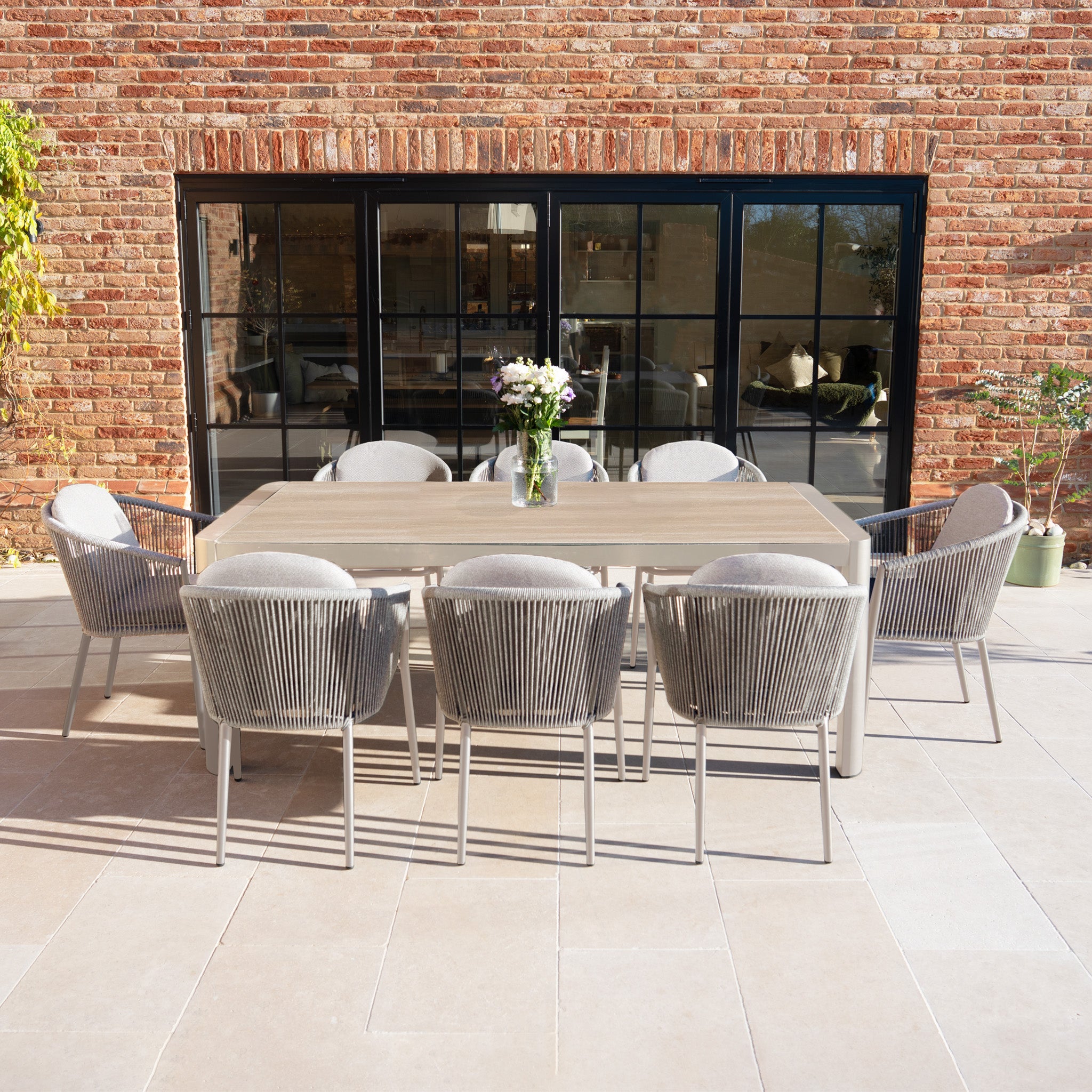 The Ravona 8 Seat Rope Extending Dining Set (162-222cm) in Latte features a spacious outdoor dining table and eight rope chairs, perfect for patios and garden gatherings.