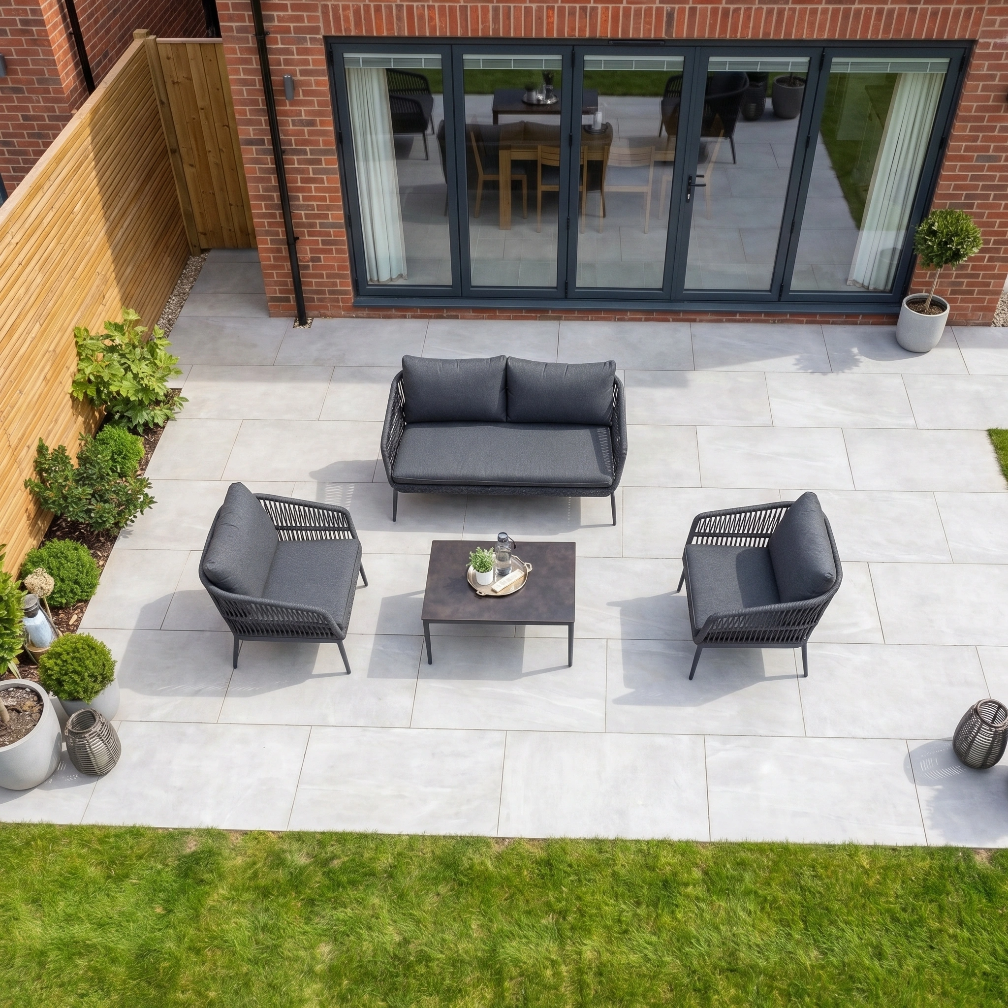 Modern outdoor patio with the stylish Rhea 2 Seat Sofa Set in Grey, a coffee table, and potted plants on large gray tiles beside the house, creating a chic space with aluminium garden furniture.