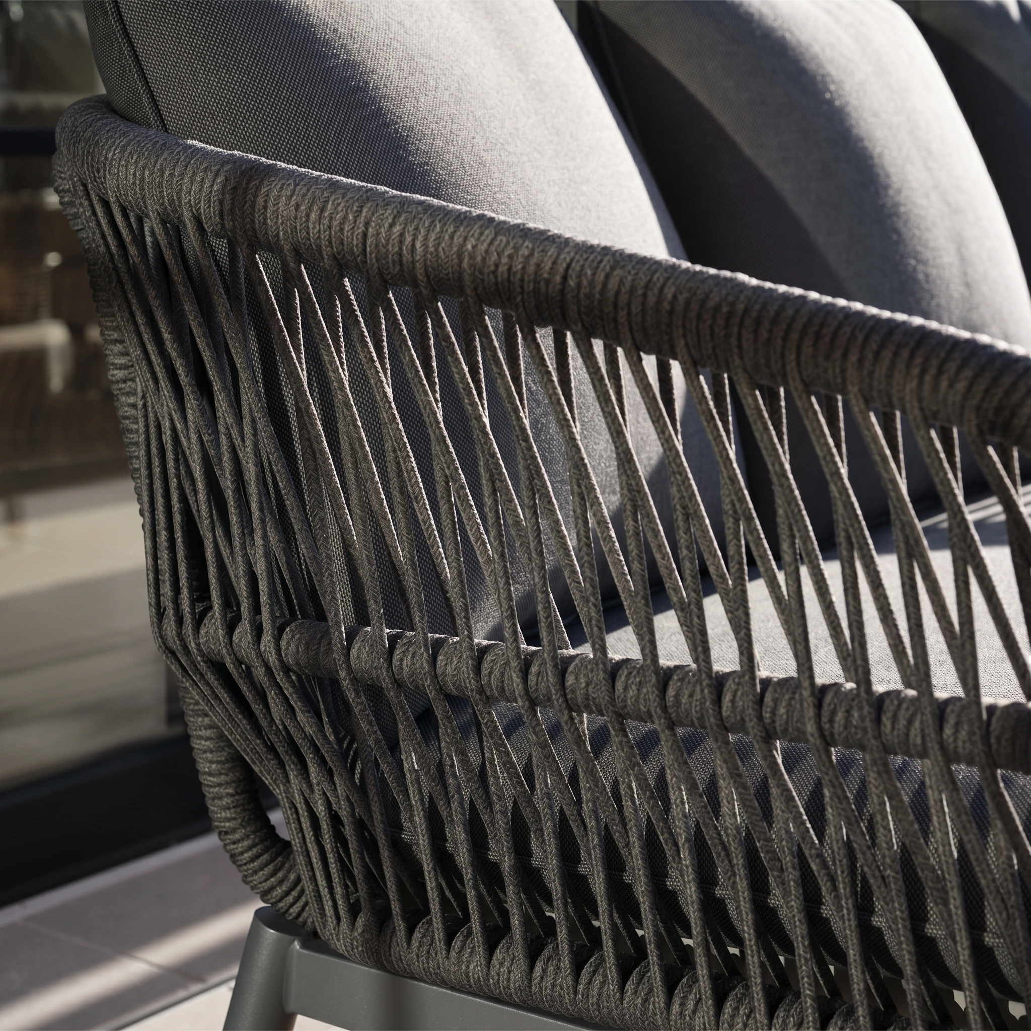 Close-up of the Rhea 2 Seat Sofa Set in Grey, a modern outdoor piece with dark woven rope sides, grey cushions, and an aluminium frame, shown basking in sunlight.