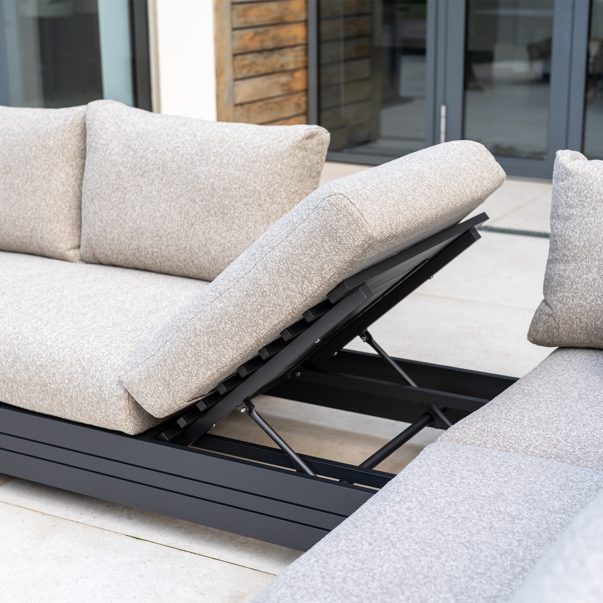 A close-up of the Savona Luxury Outdoor Large Corner Sofa Set in Truffle with an Altura Rising Table, featuring adjustable reclining backrests, on a patio.