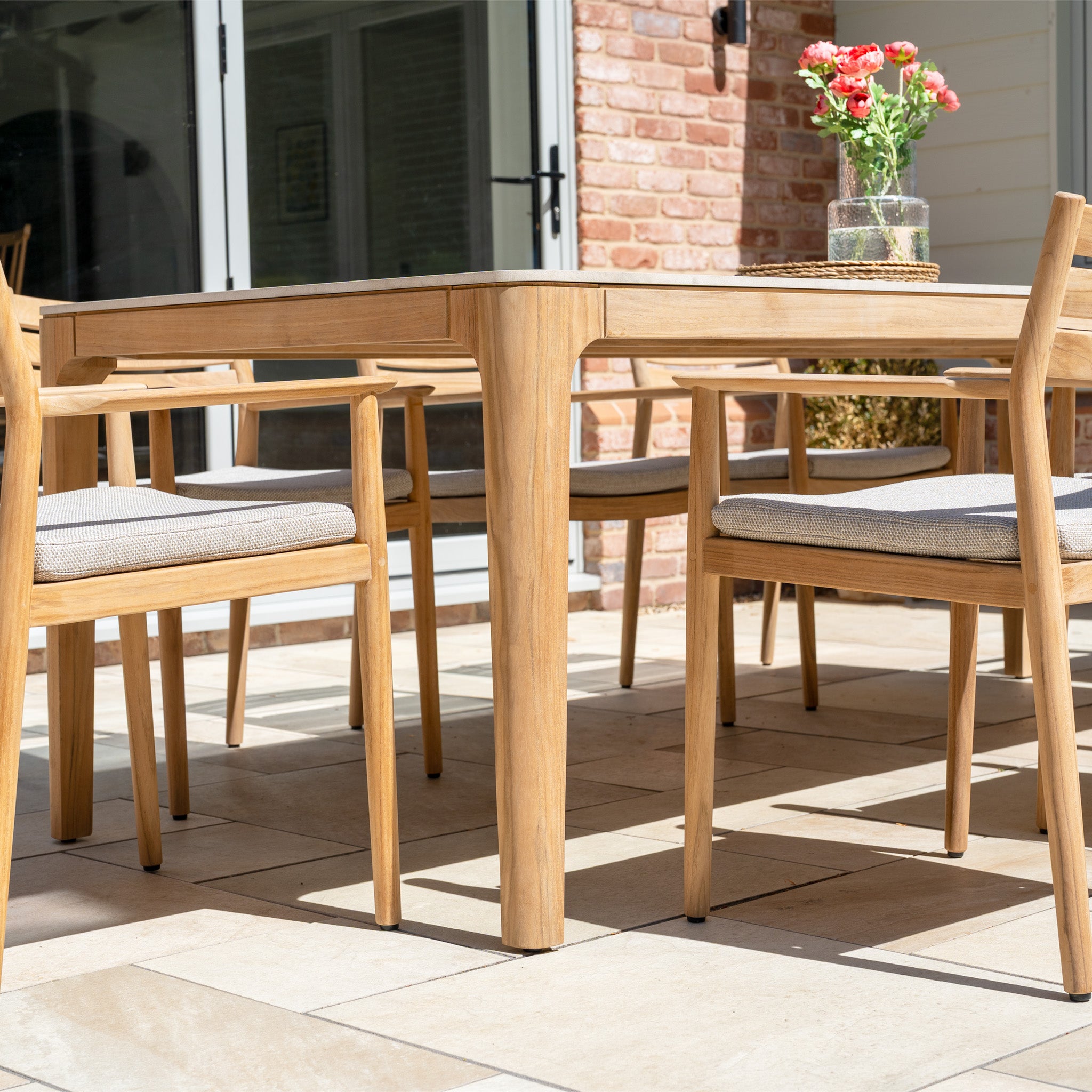 The Siena 8 Seat Dining Set with Ceramic Top Table in Fawn sits elegantly on a tiled outdoor patio, offering spacious and stylish seating for gatherings.