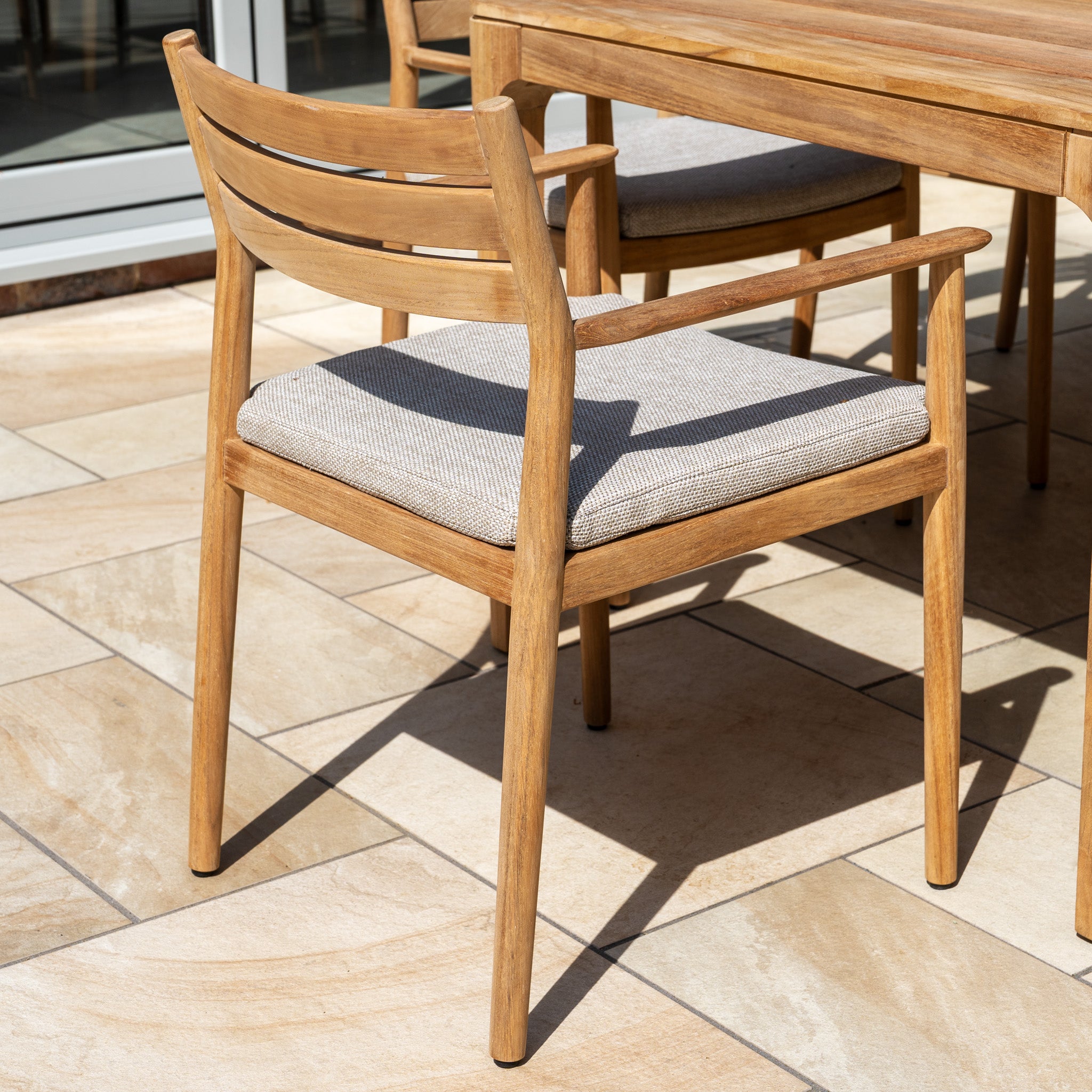 Siena 8 Seat Dining Set with Teak Table in Fawn—featuring a wooden chair with light gray cushion beside a matching table—makes perfect outdoor furniture for relaxed gatherings on your patio.