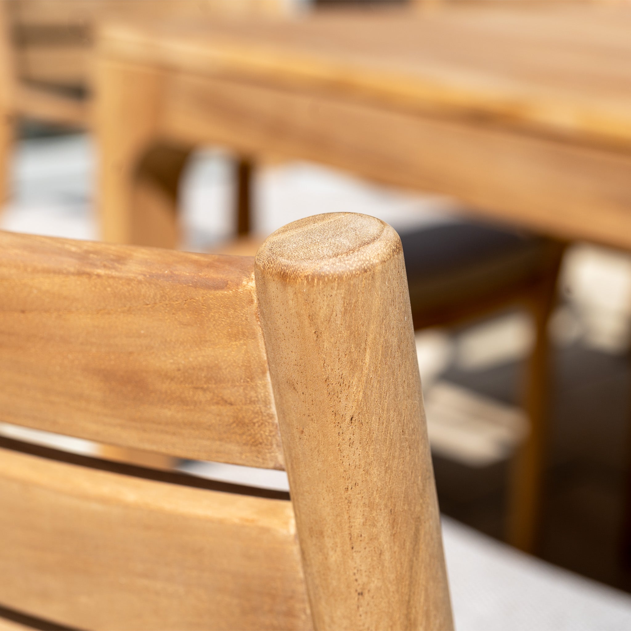 Close-up of the light wooden chair backrest from the Siena 8 Seat Dining Set with Teak Table in Fawn, with the blurred table in the background.