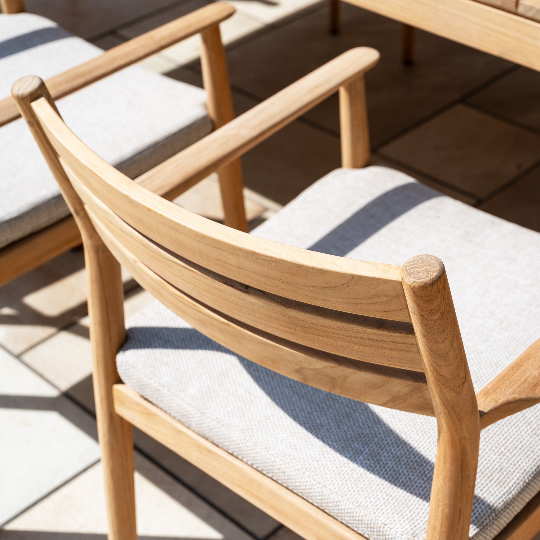 Light wooden chairs with fabric cushions encircle a Teak Table on a sunny patio—an inviting Siena 8 Seat Dining Set with Teak Table in Fawn, ideal for stylish outdoor gatherings.