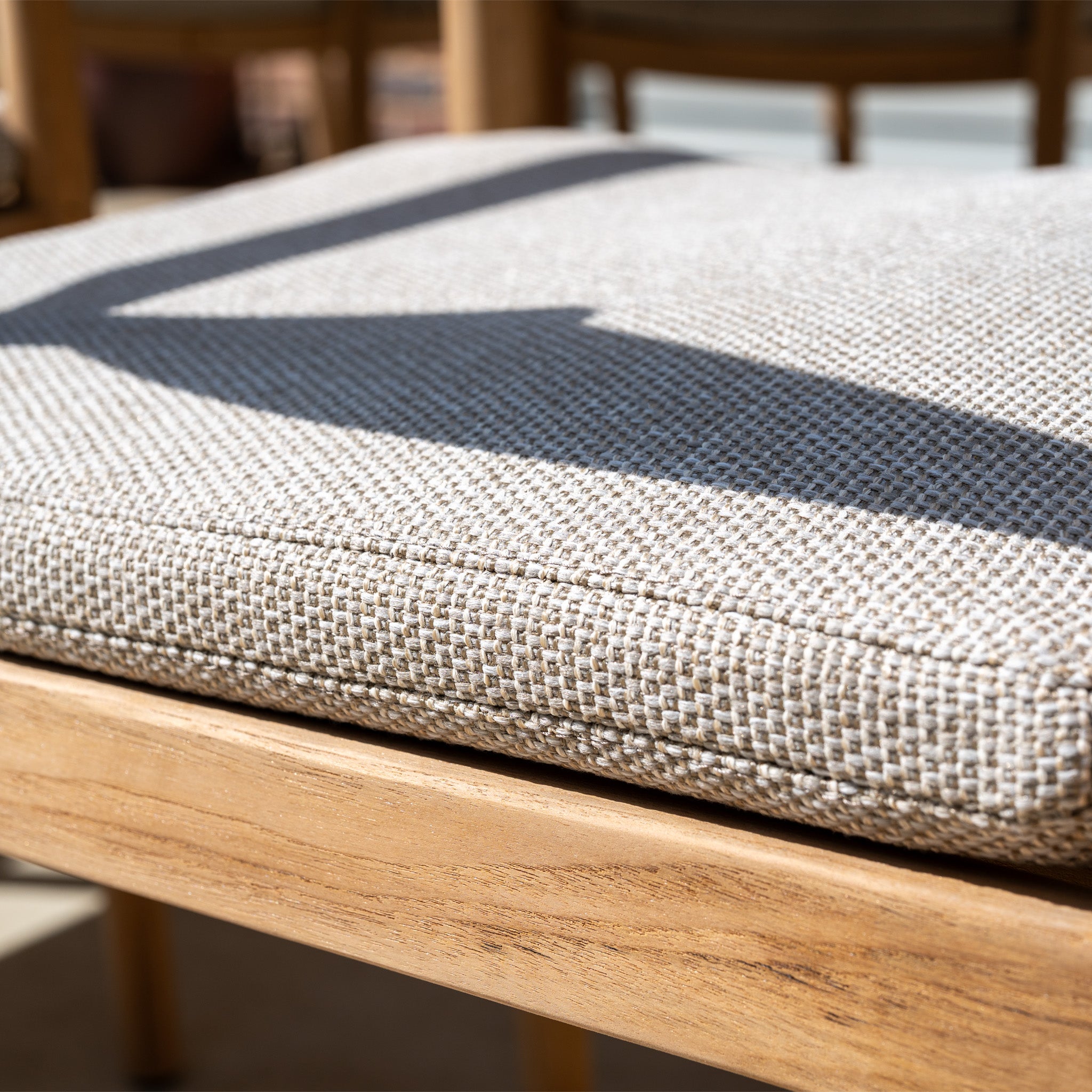 Close-up of a beige textured cushion on a wooden chair from the Siena 8 Seat Dining Set with Teak Table in Fawn, sunlight highlighting its elegant outdoor design.