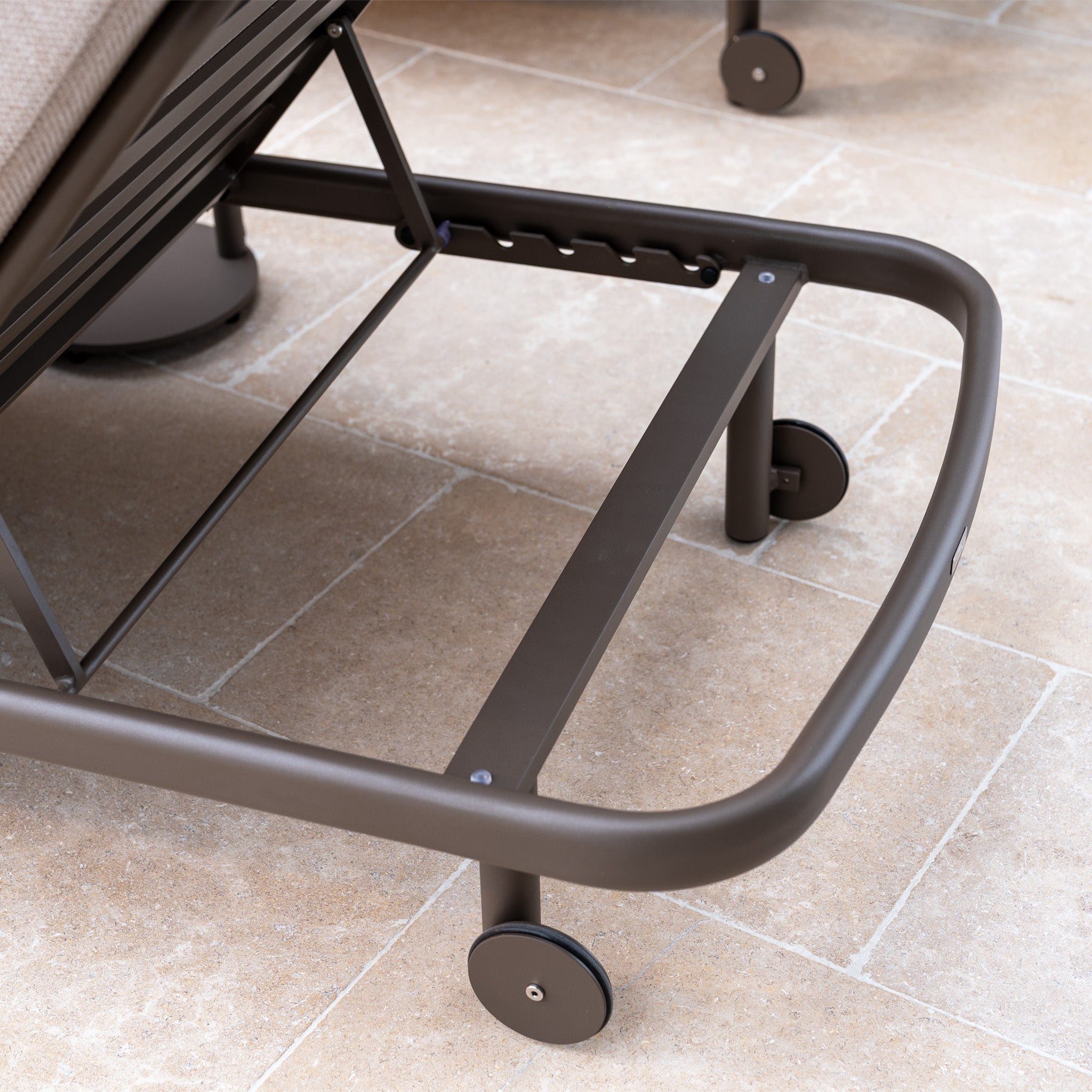 Close-up of the metal frame and wheels of the Sofia Sunlounger with Headrest and Wheels in Putty, shown on beige tile flooring.