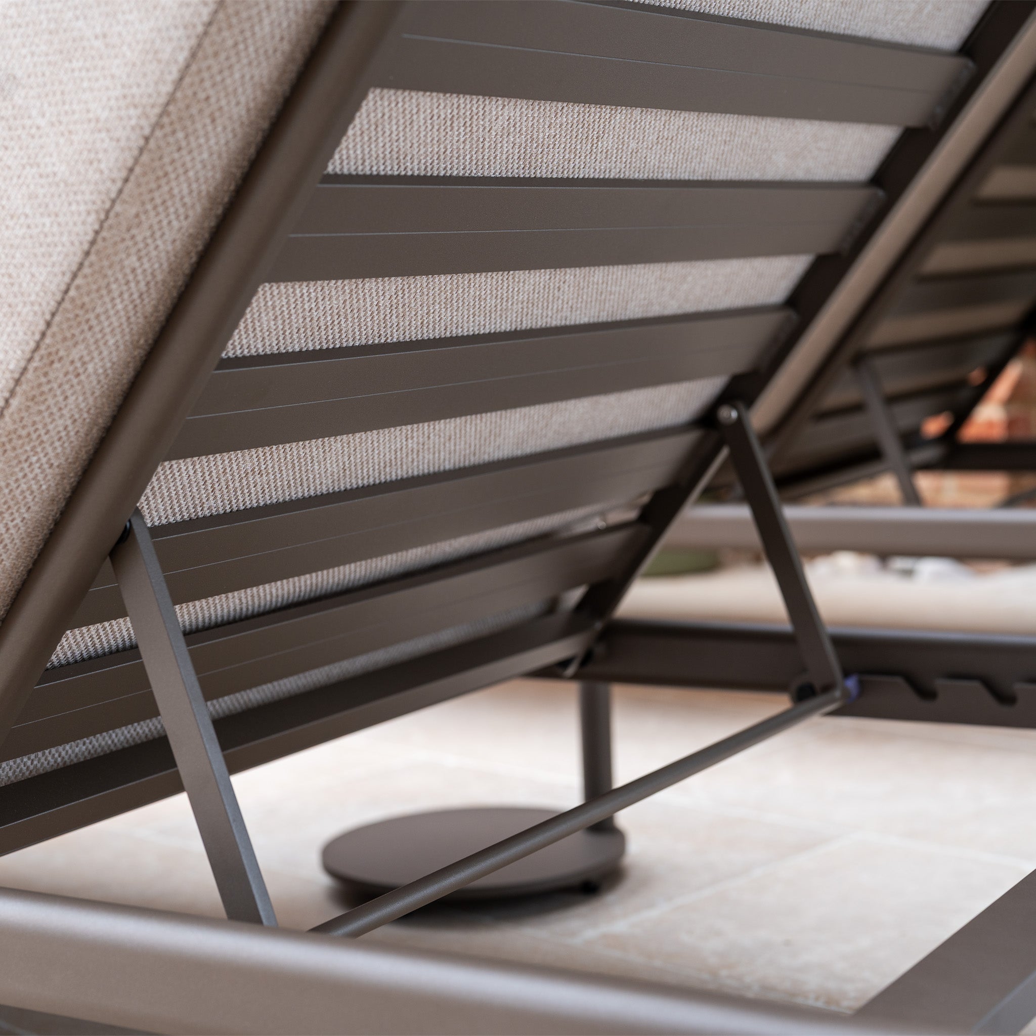 Close-up of the metal frame and adjustable backrest of the Sofia Sunlounger with Headrest and Wheels in Putty, shown on a tiled surface.