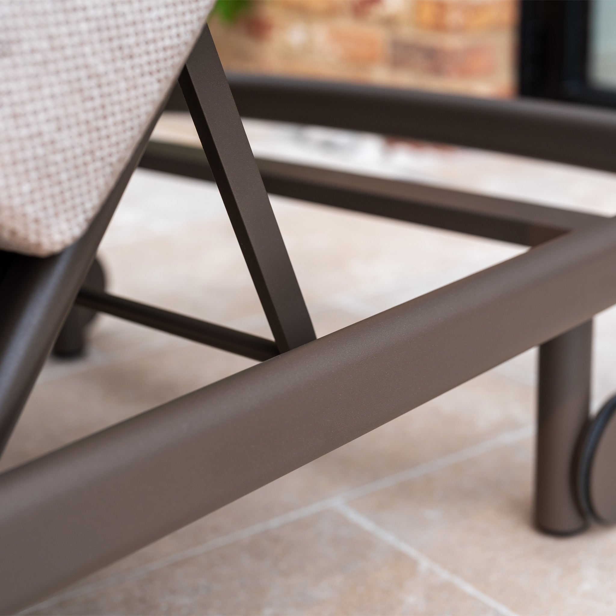 Close-up of the Sofia Sunlounger with Headrest and Wheels in Putty on a tiled patio floor.