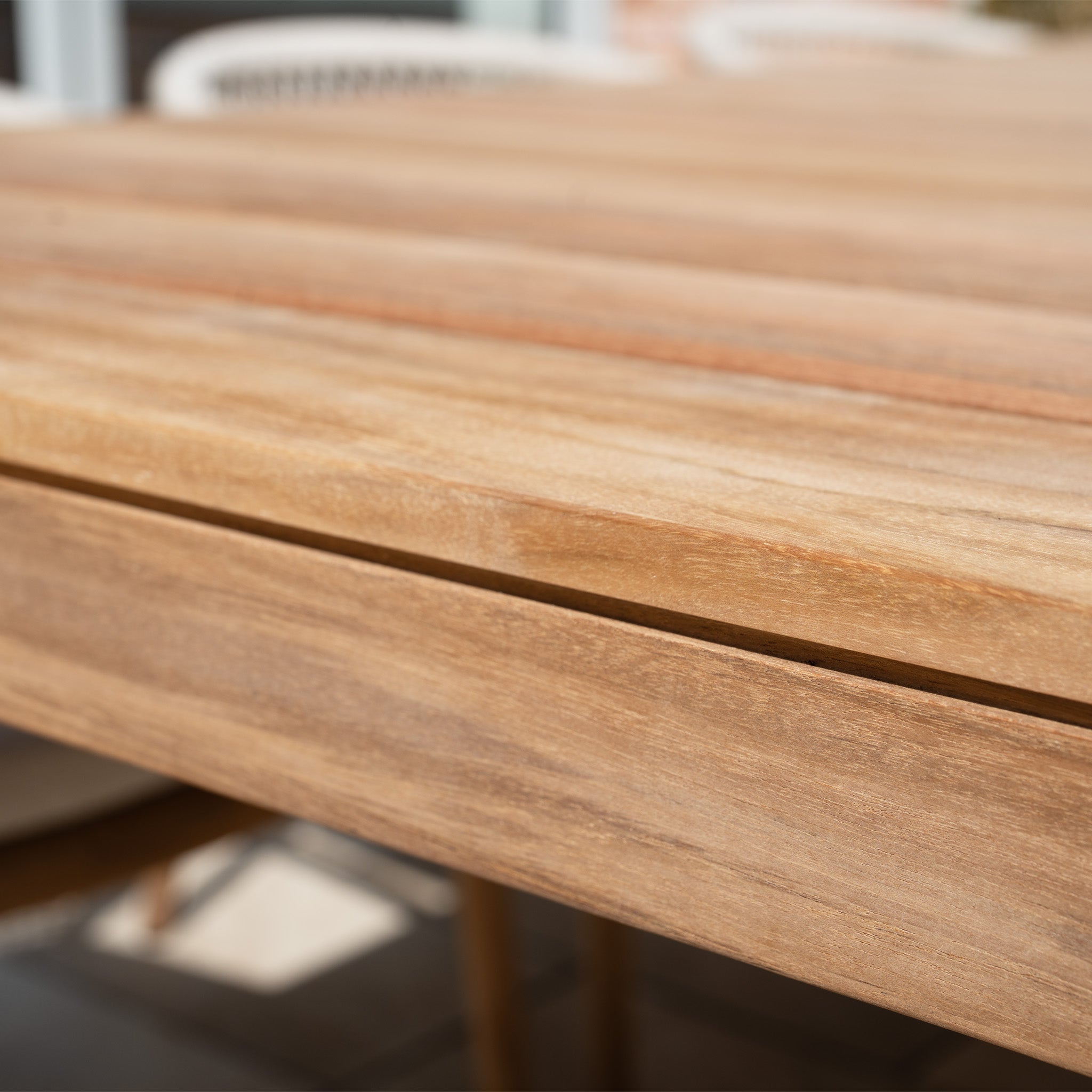 Close-up of the Sora 8 Seat Rope Dining Set with Teak Table in Stone, showing the slatted teak table surface and blurred chairs in the background.