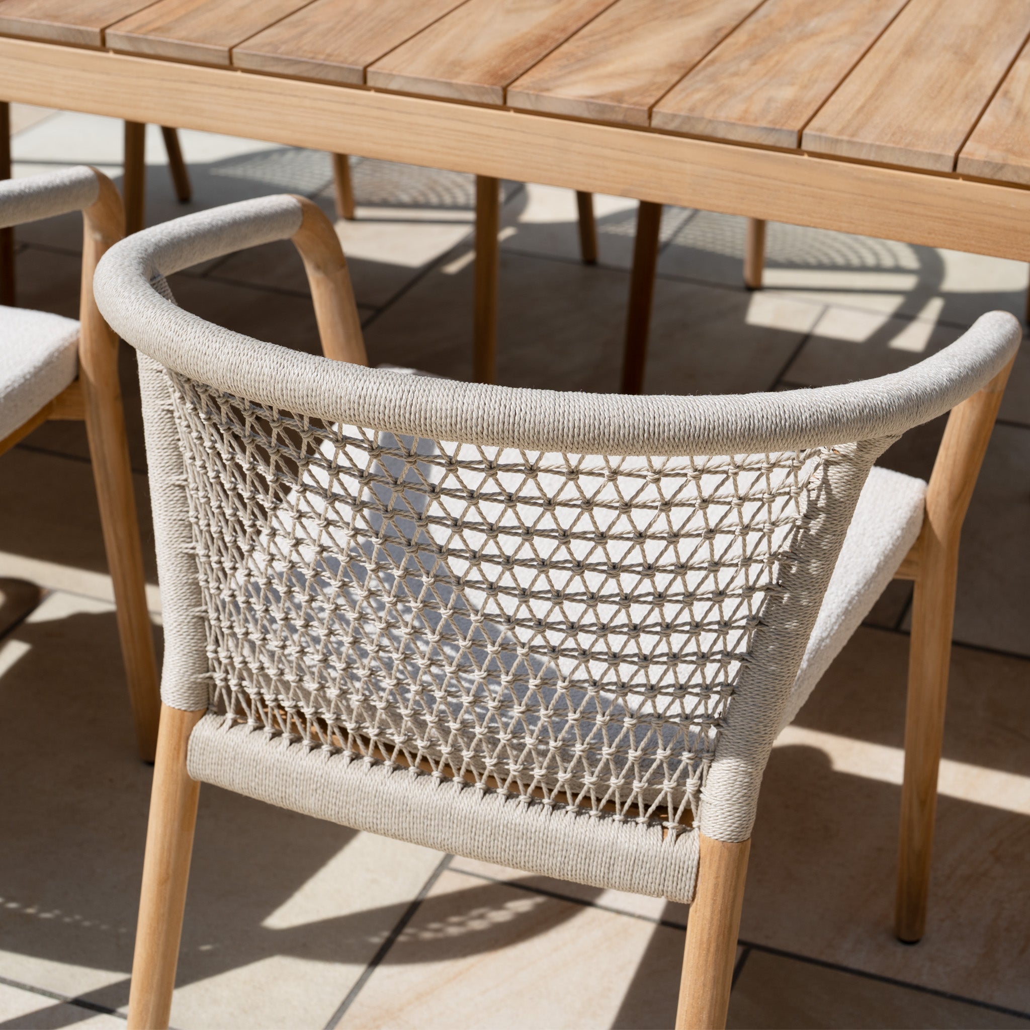 The Sora 8 Seat Rope Dining Set with Teak Table in Stone features handwoven rope chairs and a sturdy teak table, perfect for creating an inviting outdoor setting on your tiled patio.