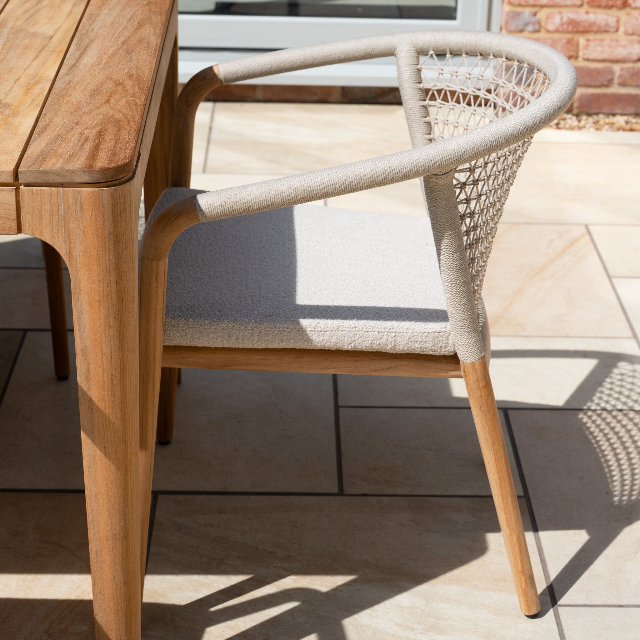 The Sora 8 Seat Rope Dining Set with Teak Table in Stone features handwoven rope chairs and a matching teak table, creating a stylish outdoor dining setup on your patio.