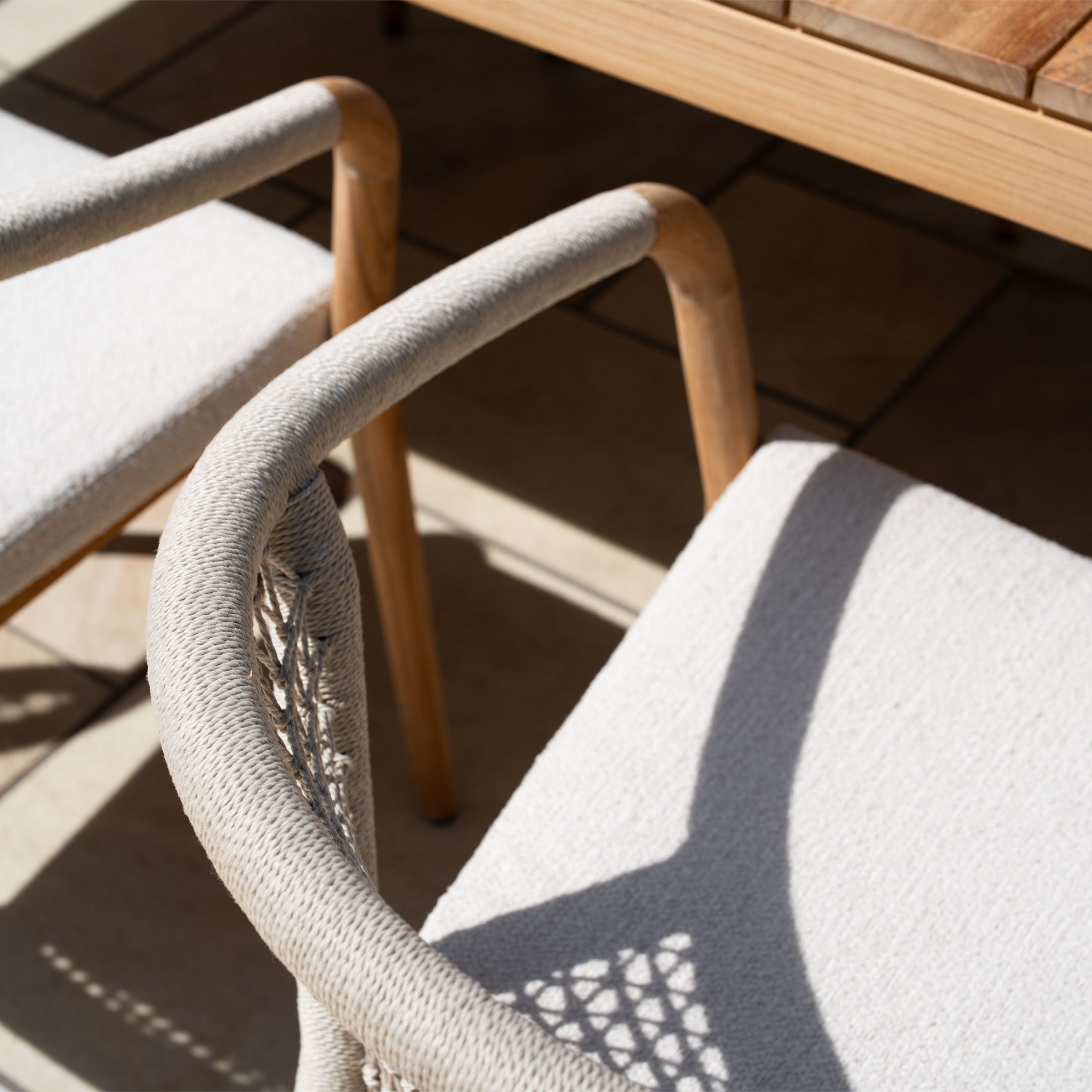 The Sora 8 Seat Rope Dining Set with Teak Table in Stone features modern, weather-resistant chairs and a teak table, creating an inviting outdoor arrangement perfect for sunny gatherings.