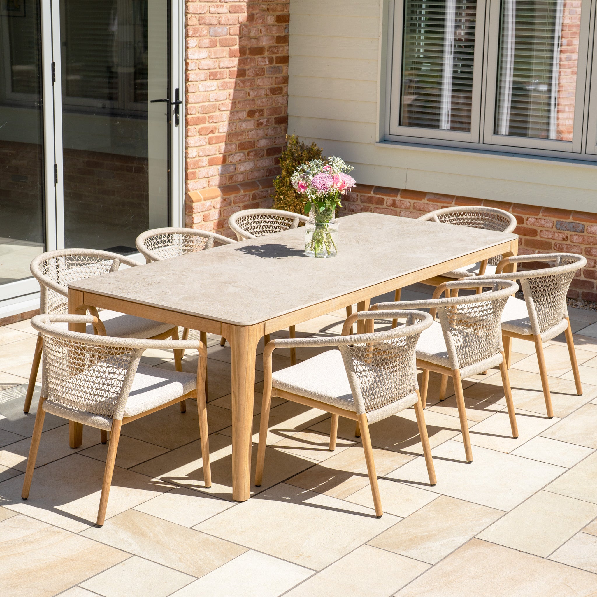 The Sora 8 Seat Rope Dining Set with Stone Ceramic Top Table features handwoven rope-accented chairs and a stylish table, perfect for alfresco dining on any patio.