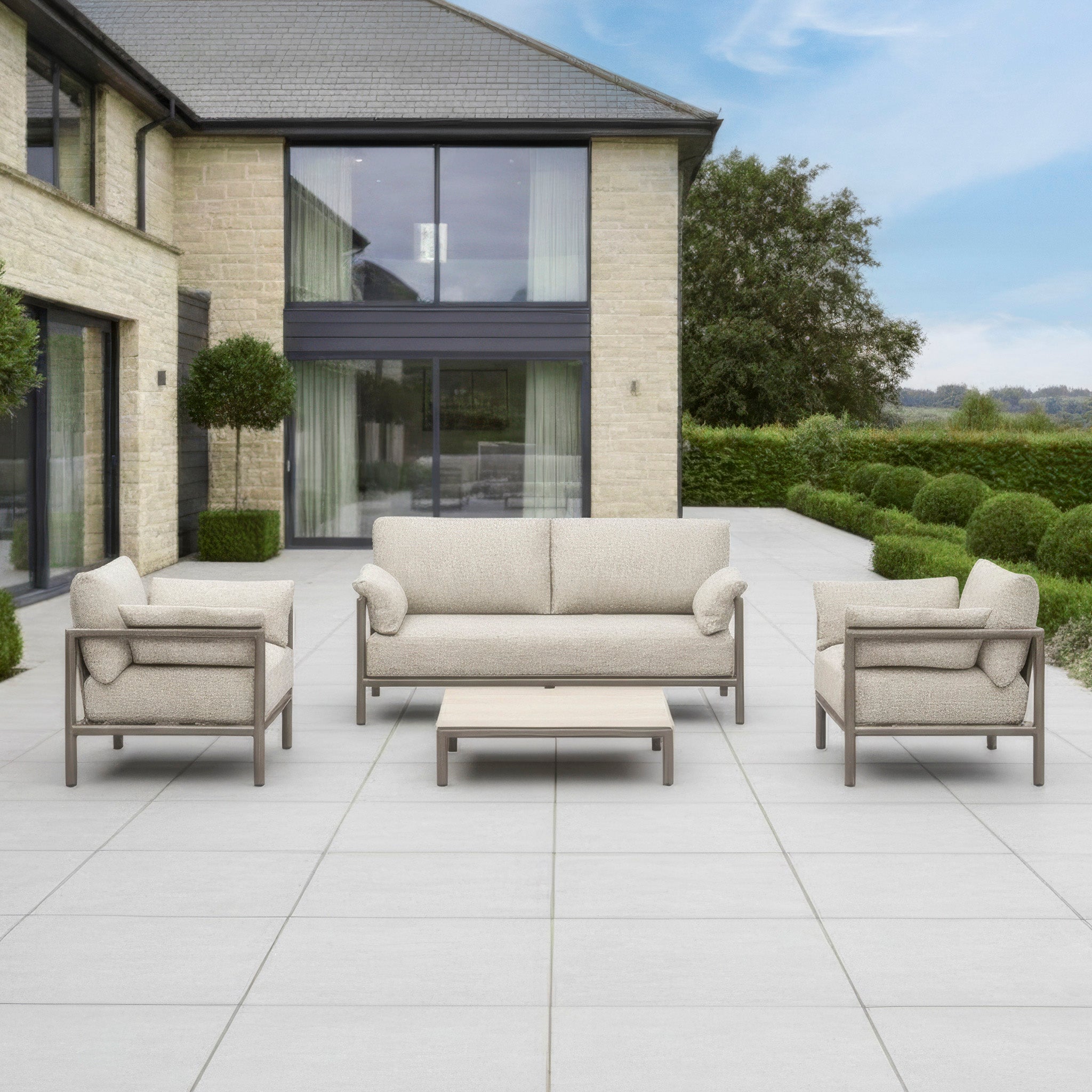 Outdoor patio with the Sorelli 2 Seat Sofa Set in Oatmeal and a matching table on a tiled terrace, placed in front of a contemporary house.