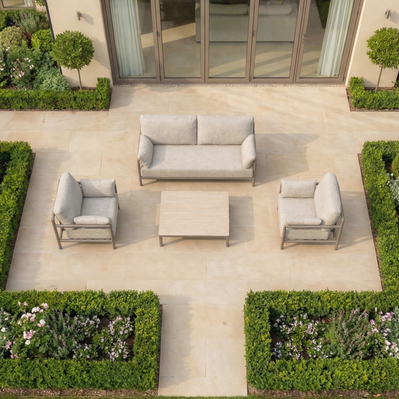 Outdoor patio features the Sorelli 2 Seat Sofa Set in Oatmeal with weather-resistant cushions, a modern coffee table, and manicured hedges in a formal garden layout.