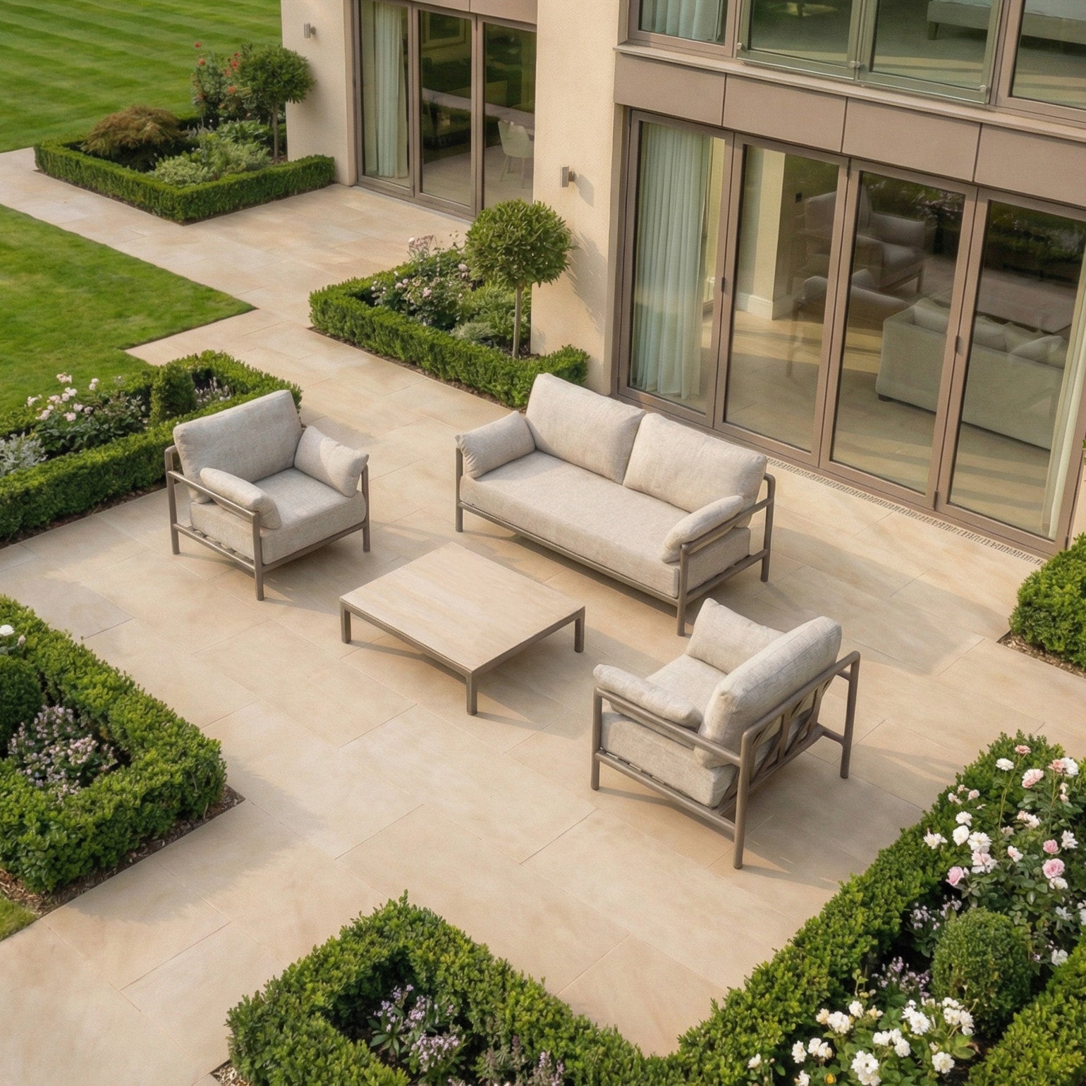 Modern patio with a Sorelli 2 Seat Sofa Set in Oatmeal, featuring weather-resistant beige furniture framed by neatly trimmed hedges and blooming flower beds.