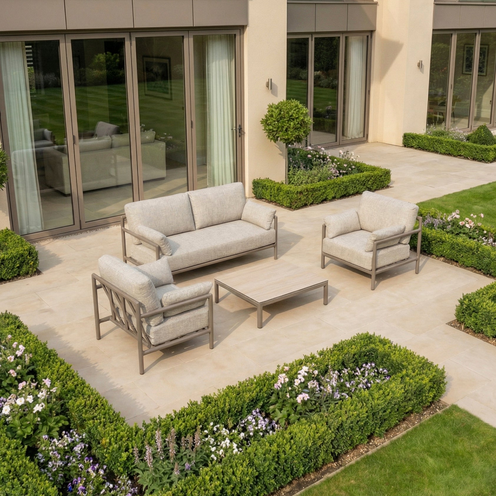 Modern patio featuring the Sorelli 2 Seat Sofa Set in Oatmeal with cushioned seating and coffee table—stylish, weather-resistant garden furniture ideal for relaxing among manicured hedges.