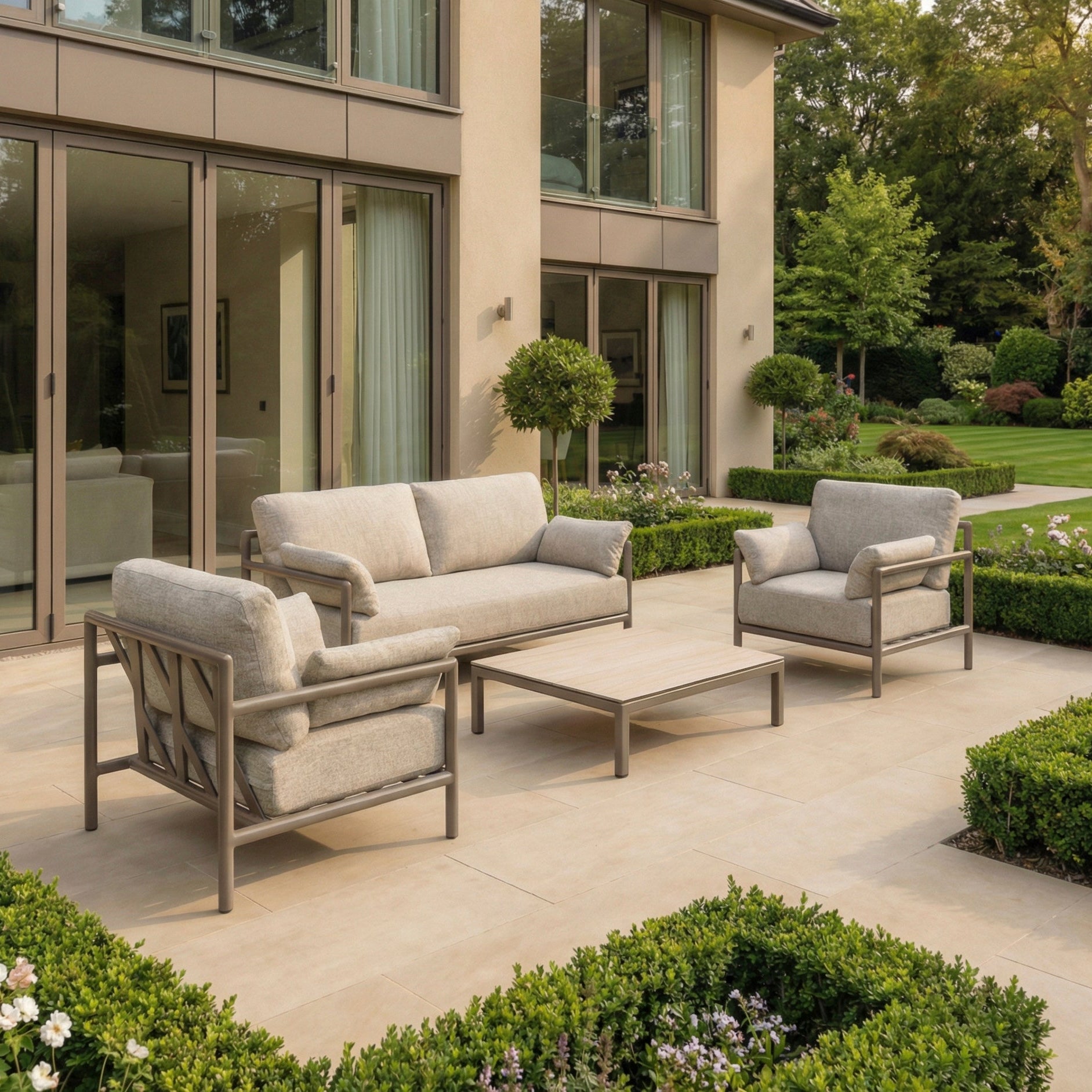 Modern outdoor patio featuring the Sorelli 2 Seat Sofa Set in Oatmeal with plush cushions and a low table, surrounded by greenery—an inviting, weather-resistant space perfect for relaxing outdoors.