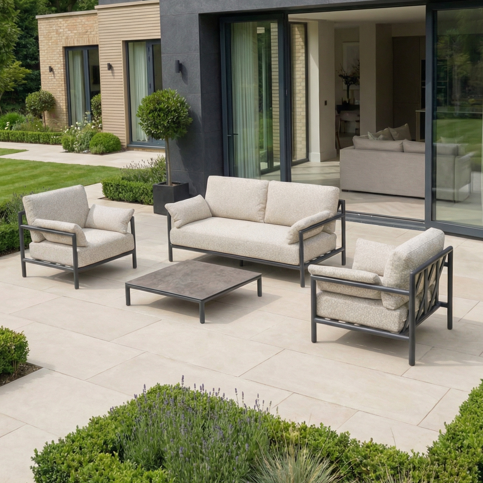 Modern patio with a Sorelli 2 Seat Sofa Set in Truffle and coffee table, beside a house with large sliding glass doors—perfect for relaxing with stylish garden furniture.