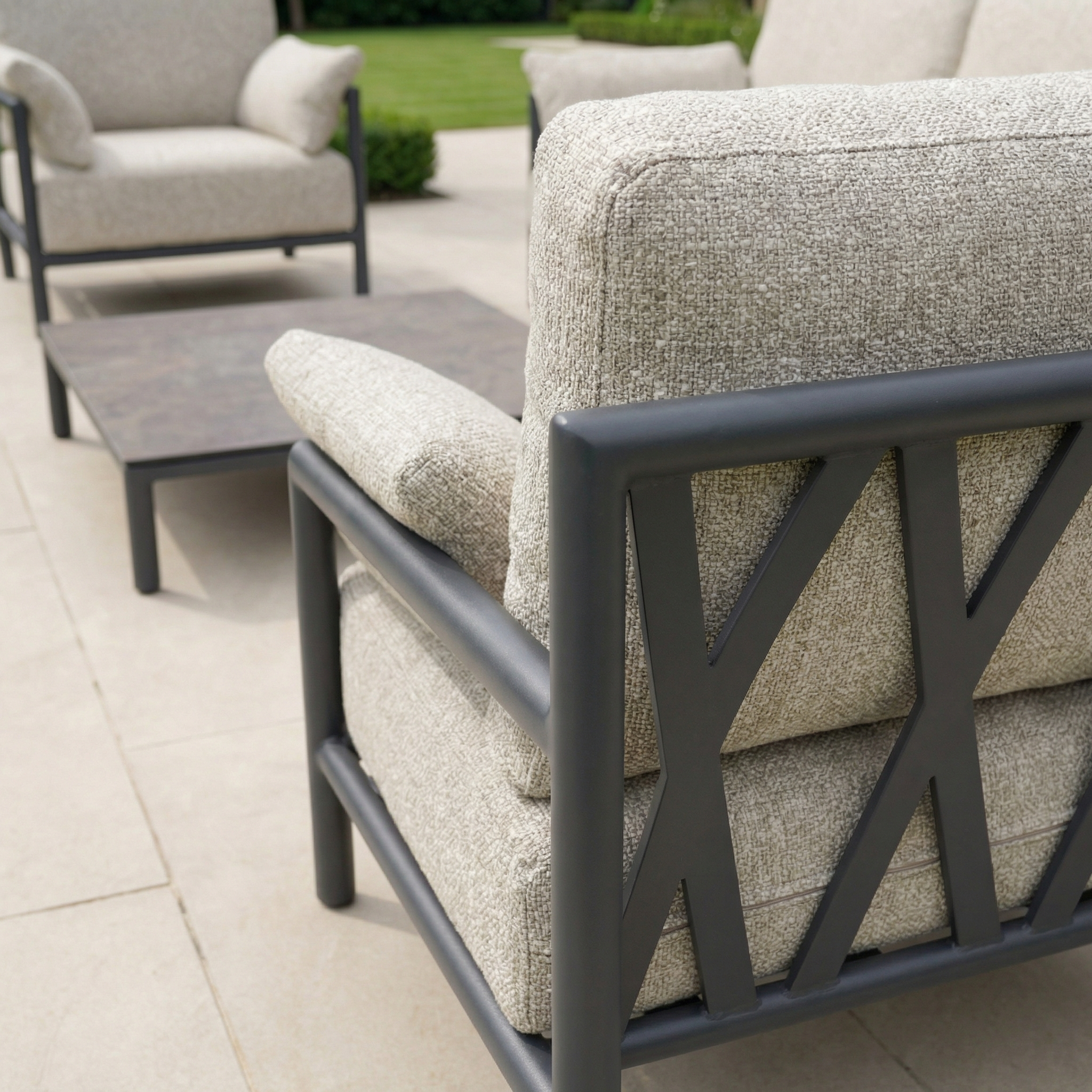 Close-up of outdoor patio chairs with beige cushions and metal frames from the Sorelli 2 Seat Sofa Set in Truffle, arranged near a low table on a stone patio for elegant outdoor relaxation.