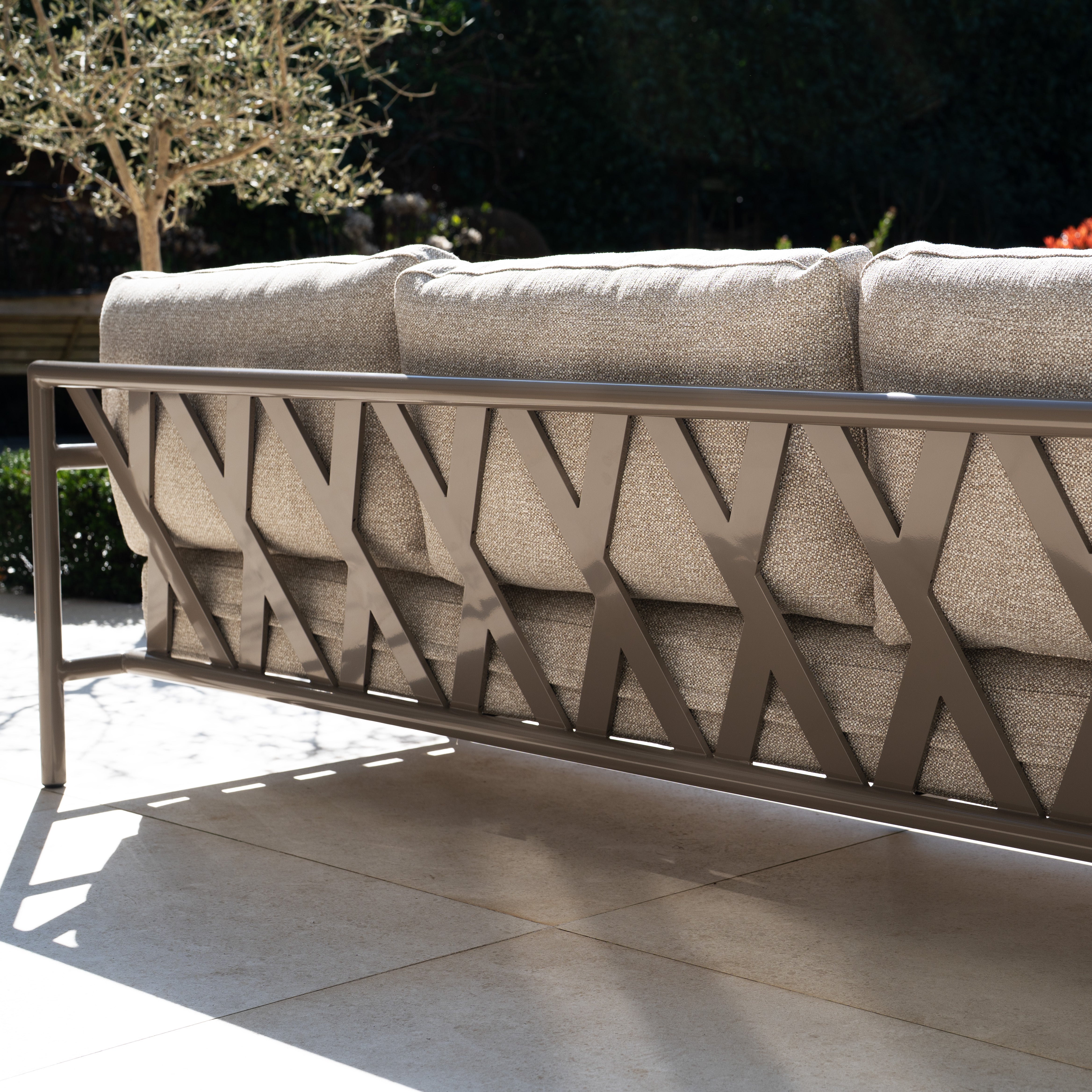 The Sorelli U Shape Corner Sofa Set in Oatmeal features a crisscross aluminium frame back and cushioned seats, perfect for relaxing on any sunlit patio.