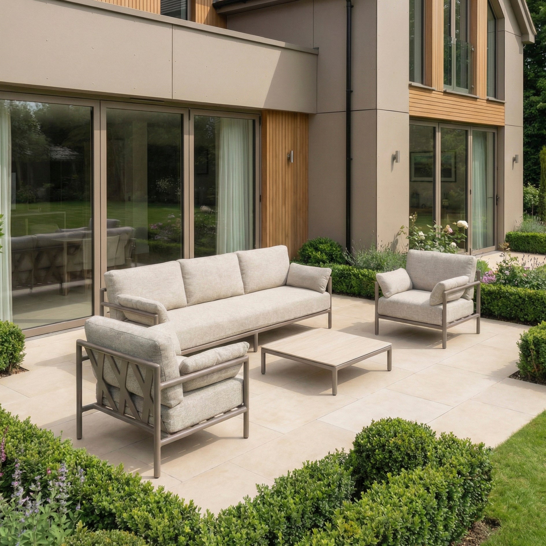 Modern patio with a weather-resistant Sorelli 3 Seat Sofa Set in Oatmeal, including a beige outdoor sofa and armchair on a tiled terrace beside a contemporary house.