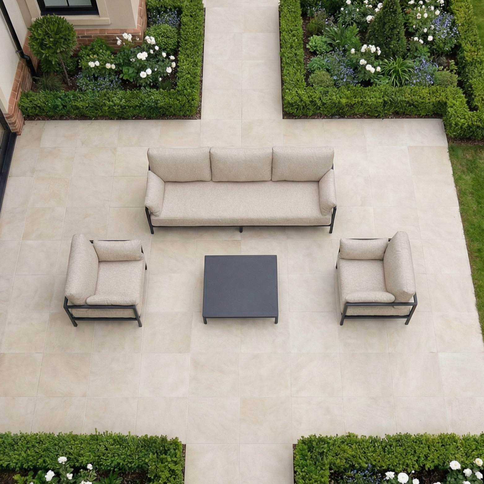 Outdoor patio featuring the Sorelli 3 Seat Sofa Set in Truffle, paired with two armchairs and a black coffee table, surrounded by lush greenery—ideal for relaxing outdoor seating.