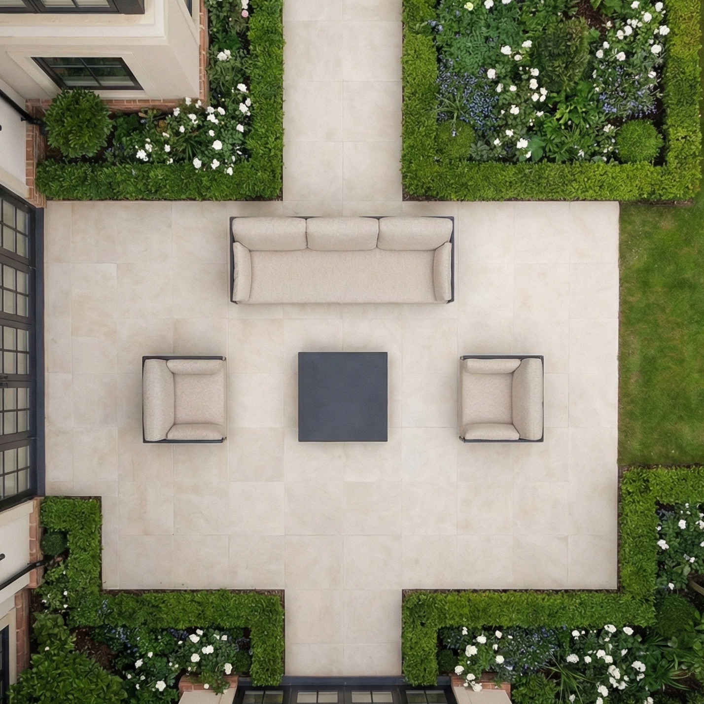 Aerial view of a patio with the Sorelli 3 Seat Sofa Set in Truffle, two chairs, a table, and lush greenery accented by vibrant flower beds.