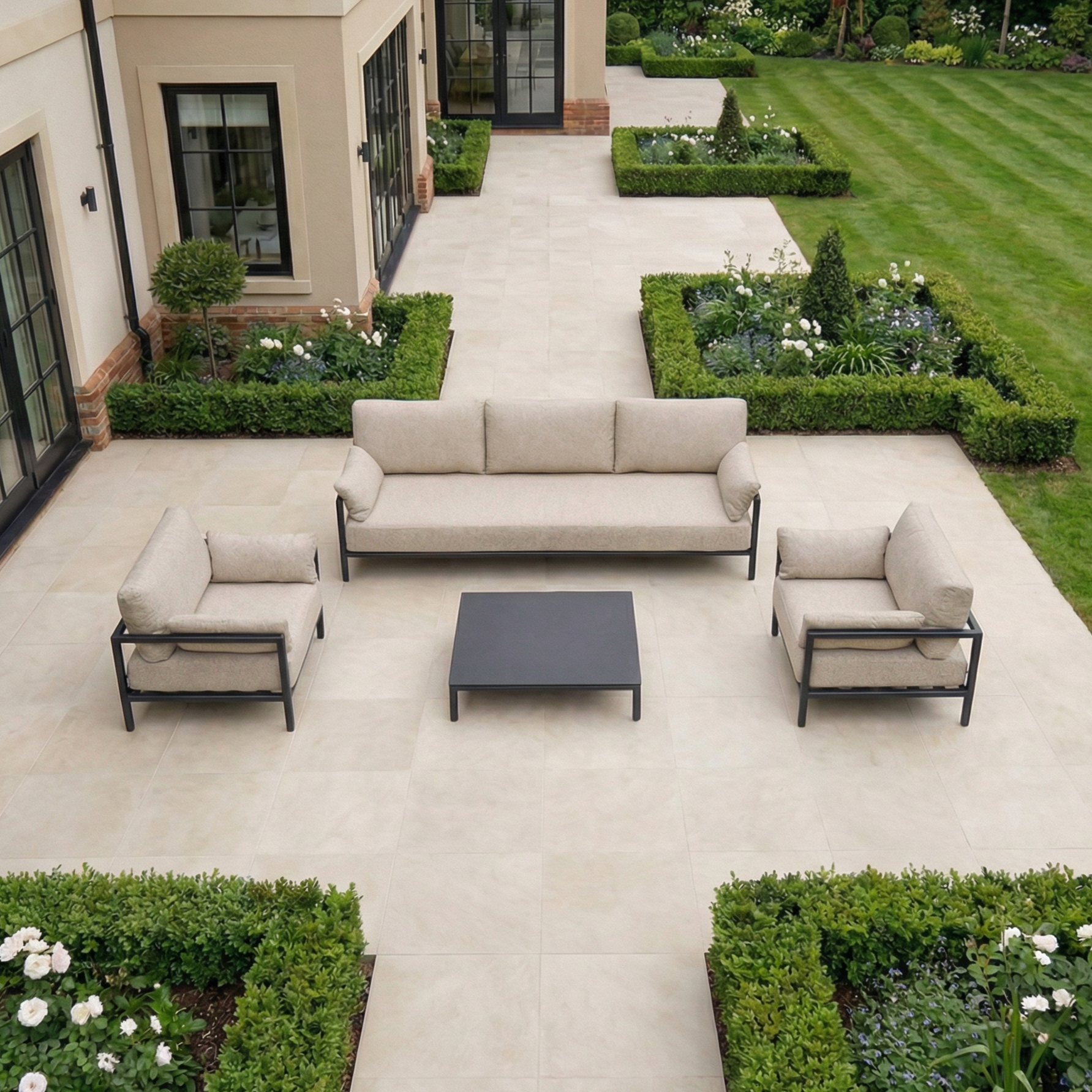 Sorelli 3 Seat Sofa Set in Truffle with a black coffee table on a tiled patio, providing stylish outdoor seating and elegant garden furniture amidst lush greenery.