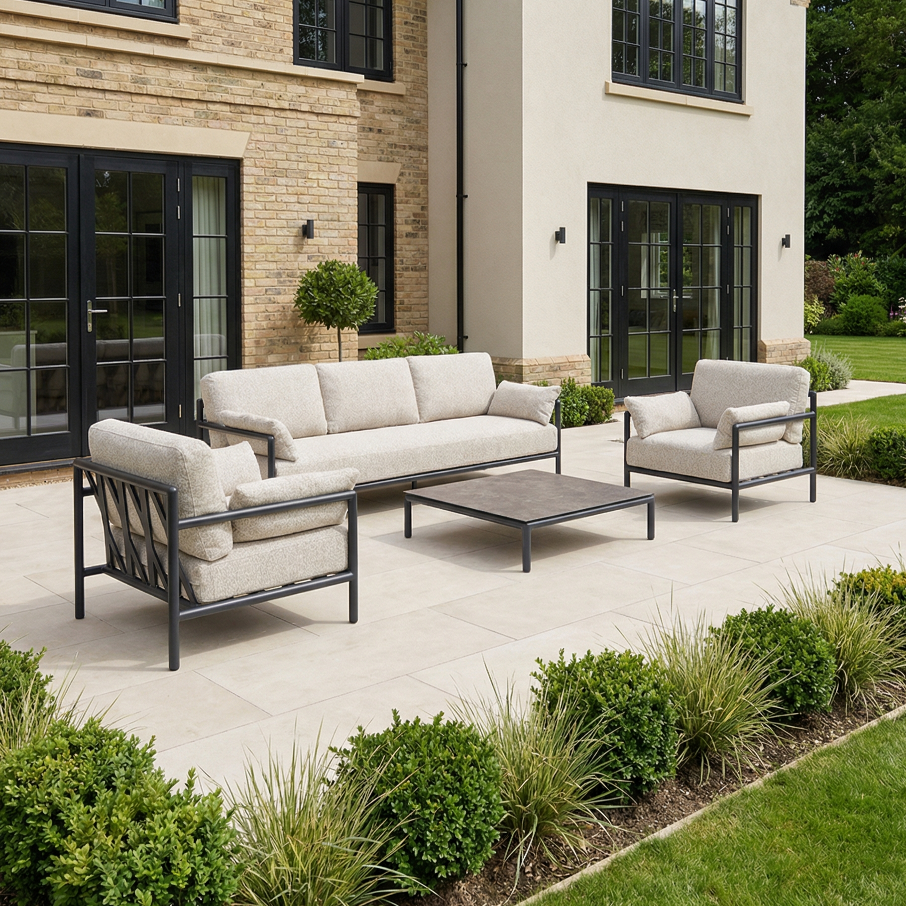 Outdoor patio featuring the Sorelli 3 Seat Sofa Set in Truffle with two chairs and a coffee table, set near a modern house and lush garden.