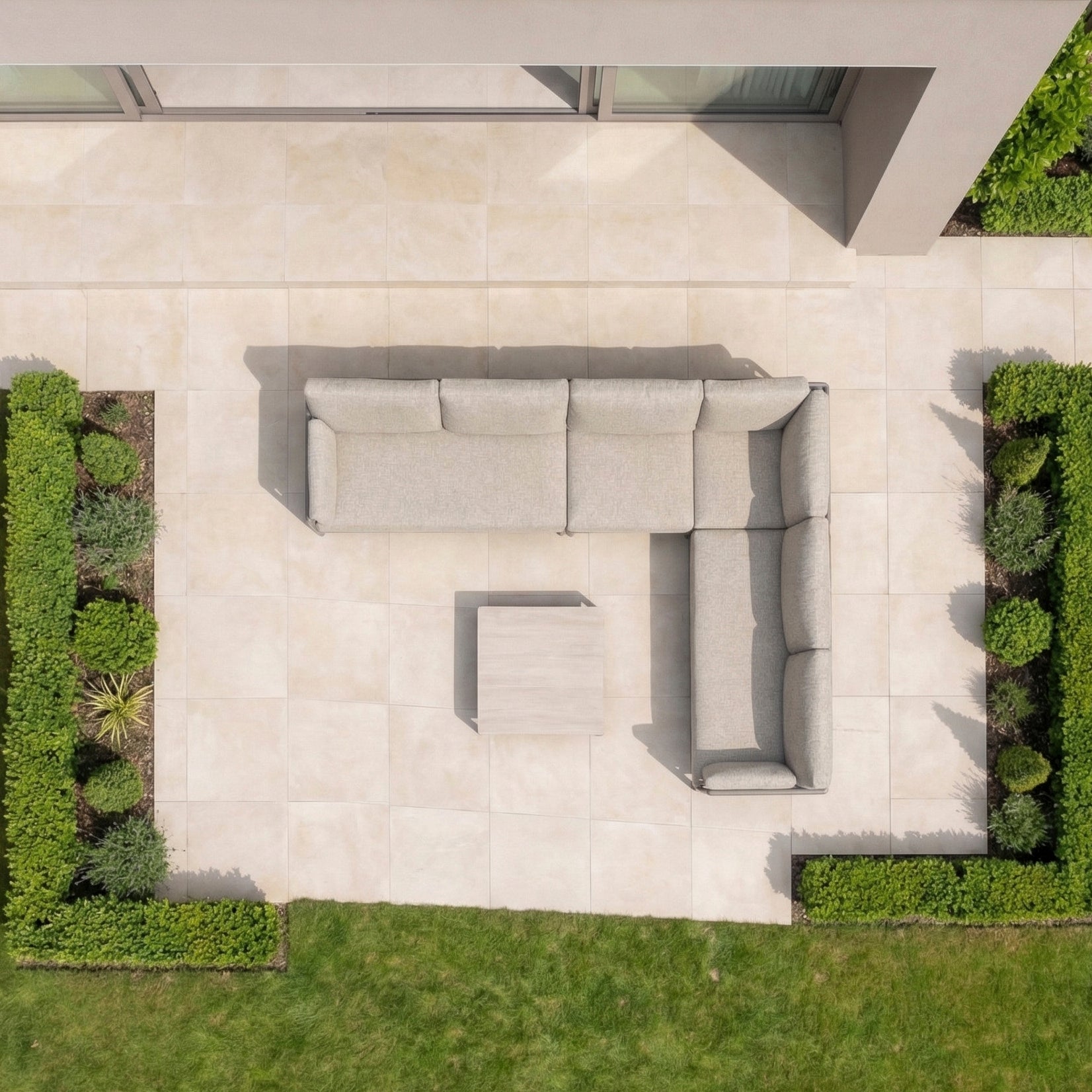 Top view of a modern patio with the Sorelli Corner Sofa Set in Oatmeal, an elegant aluminium-frame outdoor sofa paired with a square table and surrounded by neat green hedges.