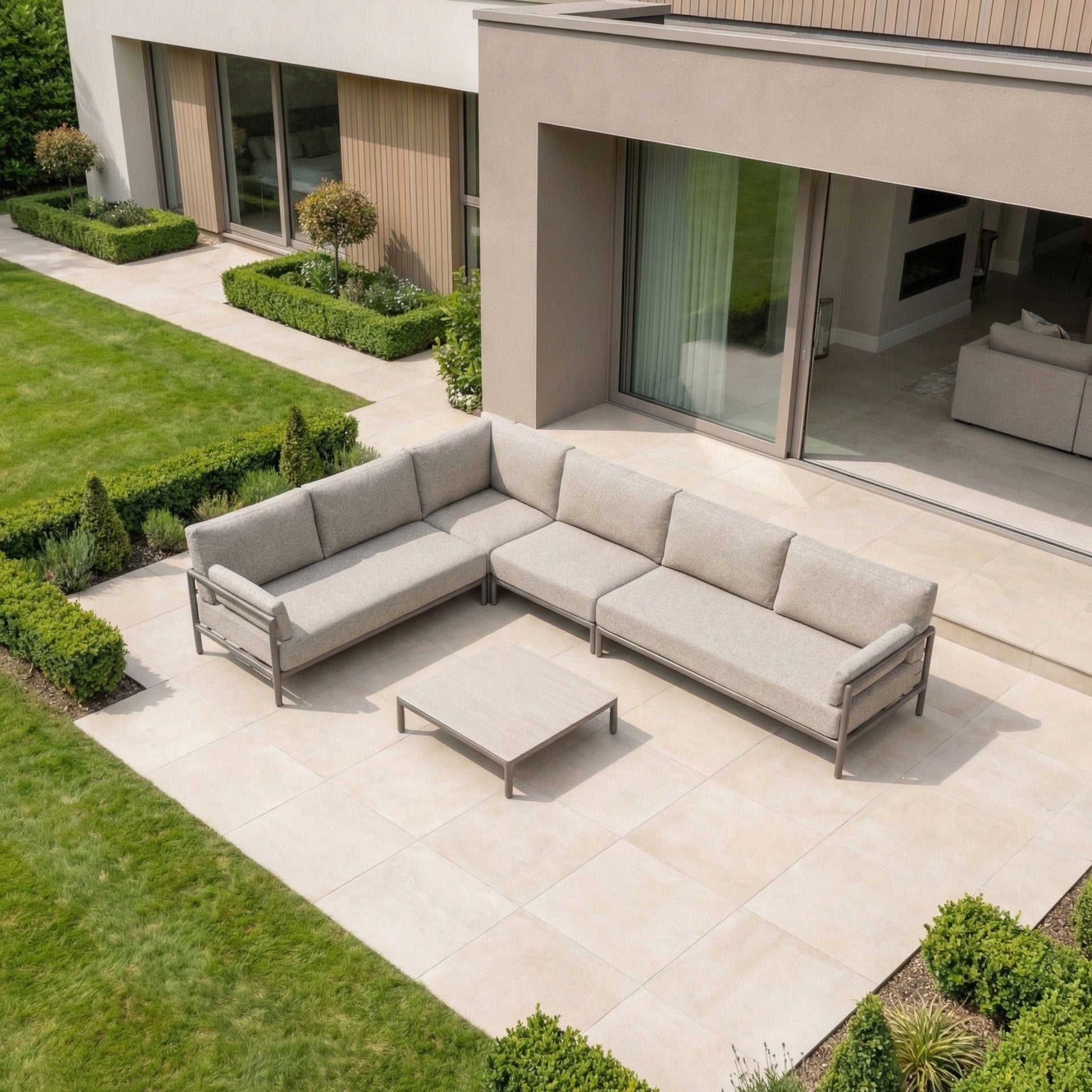 Modern outdoor patio with a Sorelli Corner Sofa Set in Oatmeal, featuring an aluminium frame and coffee table, on tiled flooring beside a contemporary house.