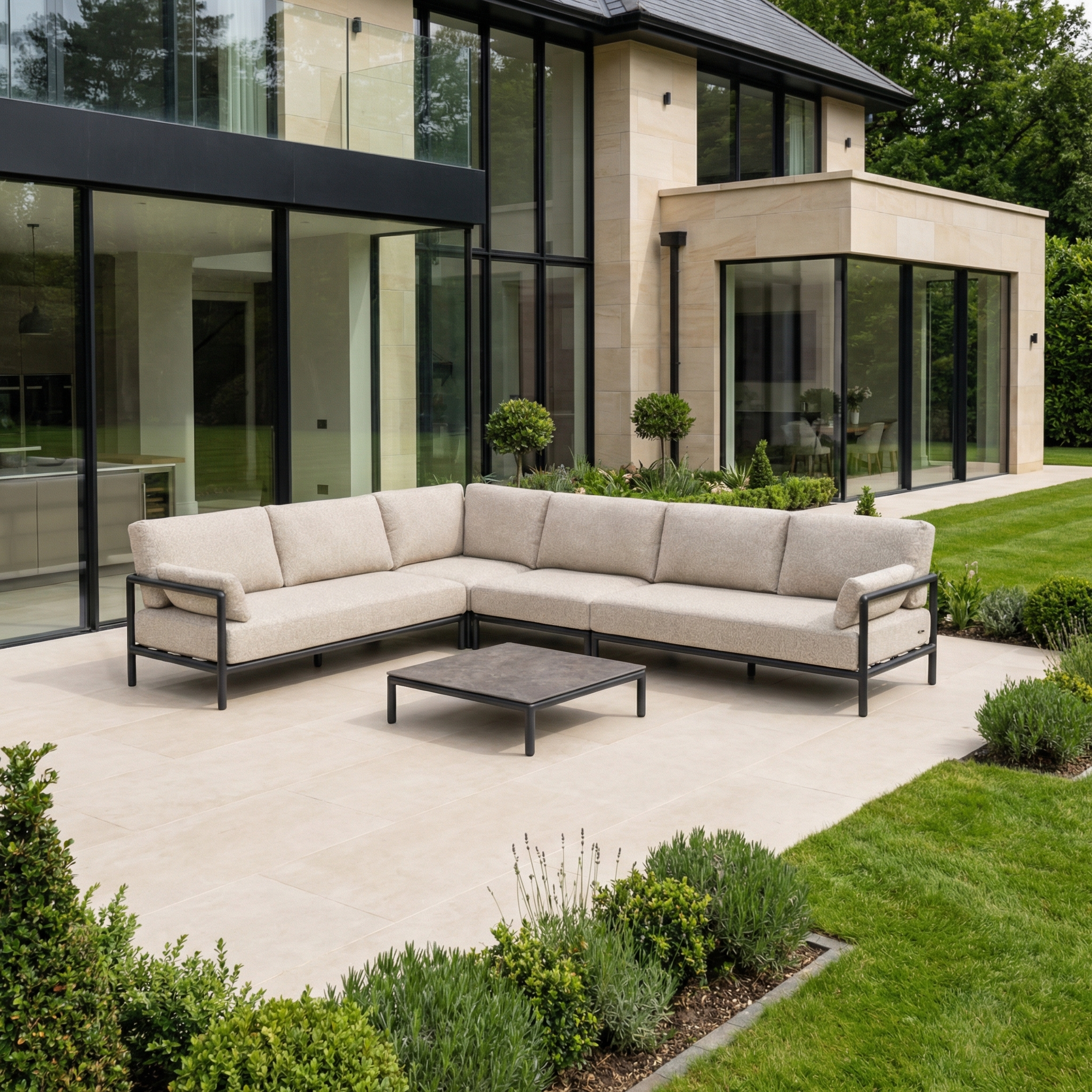 Modern outdoor patio with a Sorelli Corner Sofa Set in Truffle, a low coffee table, and a landscaped garden next to a contemporary house.