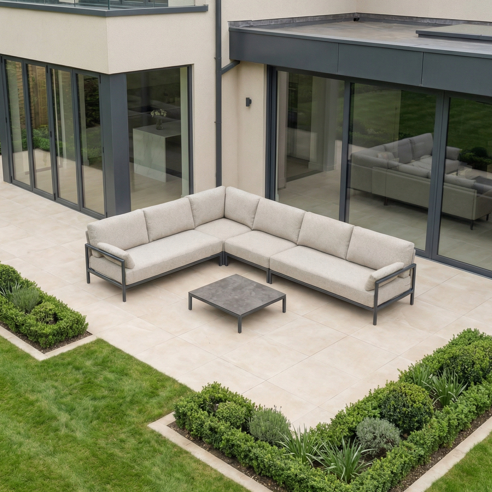 A stylish outdoor patio showcases the Sorelli Corner Sofa Set in Truffle, an L-shaped beige sofa paired with a square coffee table, all nestled amid vibrant greenery.