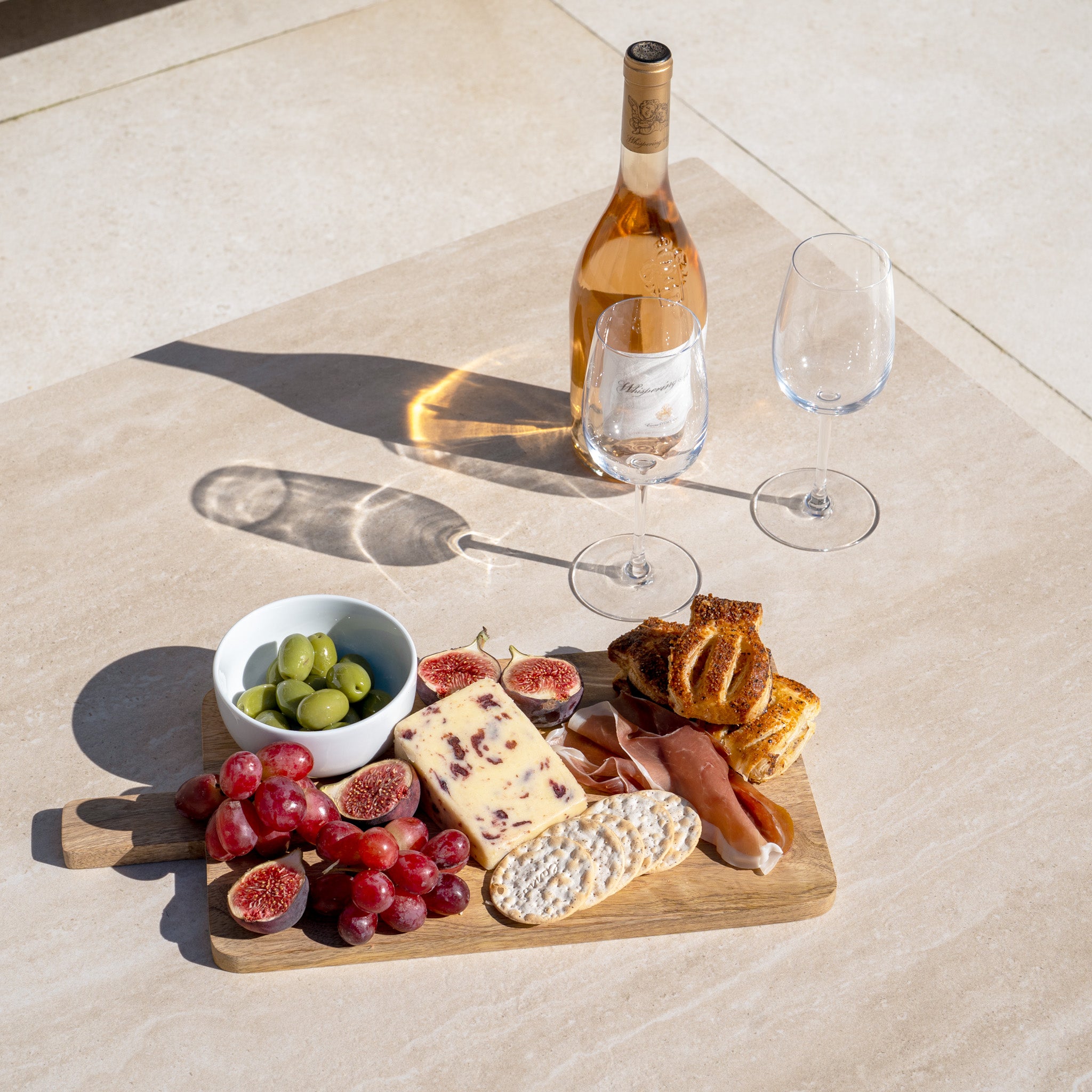 Charcuterie board with cheese, grapes, figs, olives, bread, and wine with two glasses on a sunny patio featuring the stylish Sorelli U Shape Corner Sofa Set in Oatmeal.