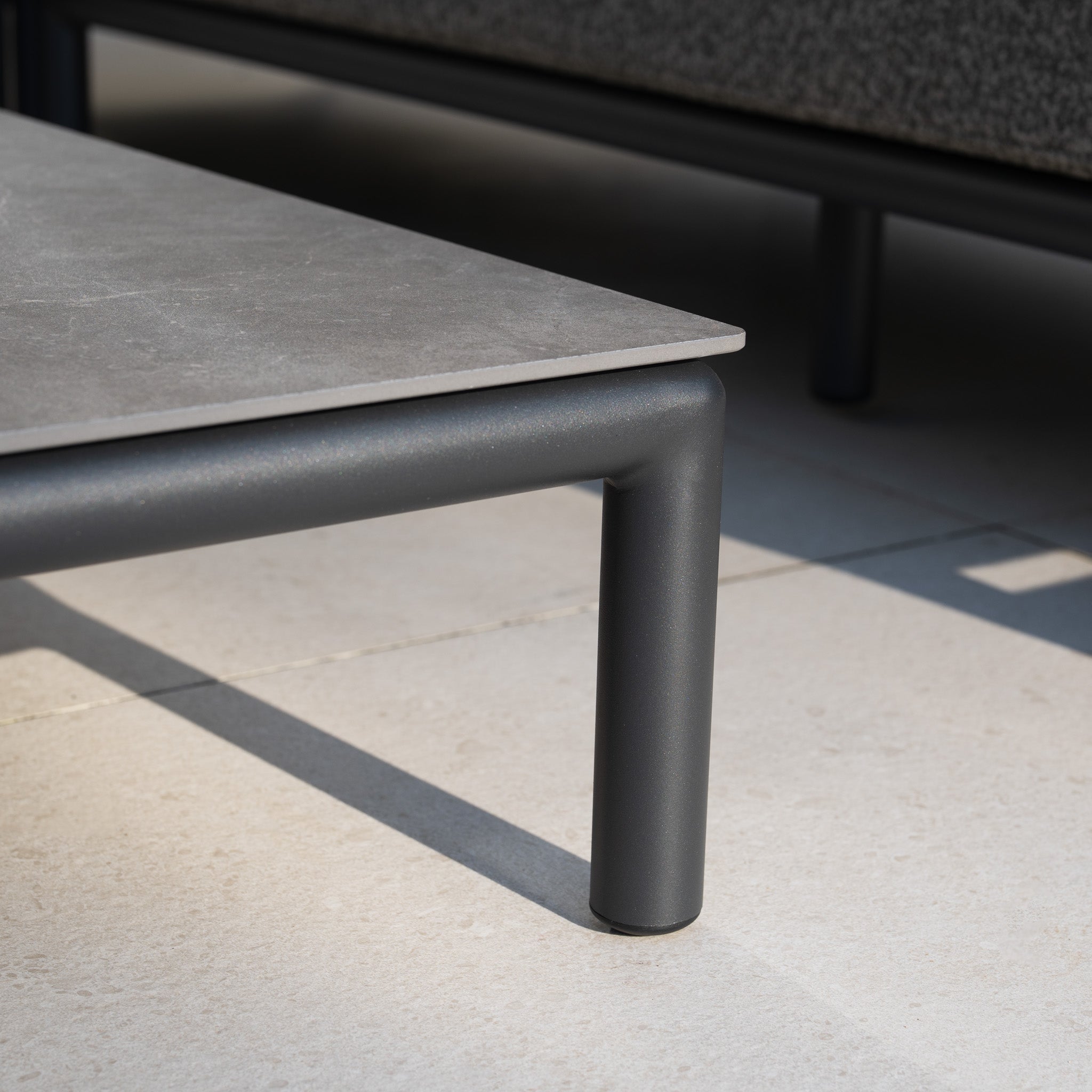 Close-up of a modern table with a gray stone top and black metal legs on a light tiled floor, perfectly complementing aluminium garden furniture like the Sorelli 2 Seat Sofa Set in Truffle.