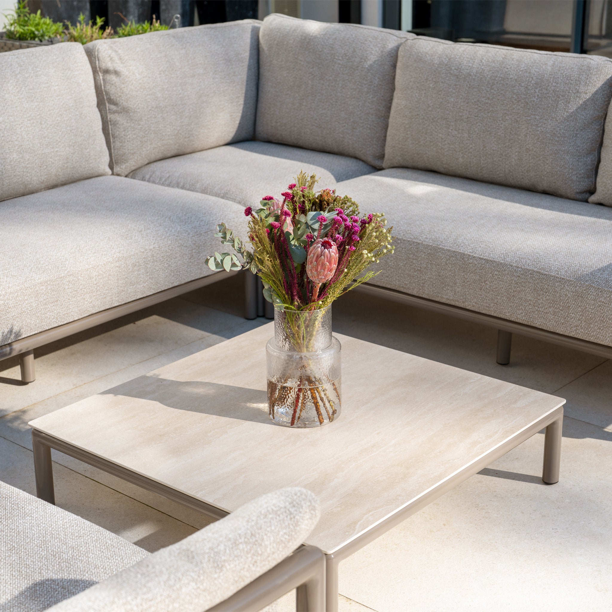 A glass vase with dried flowers sits on a square coffee table, surrounded by the Sorelli U Shape Corner Sofa Set in Oatmeal.