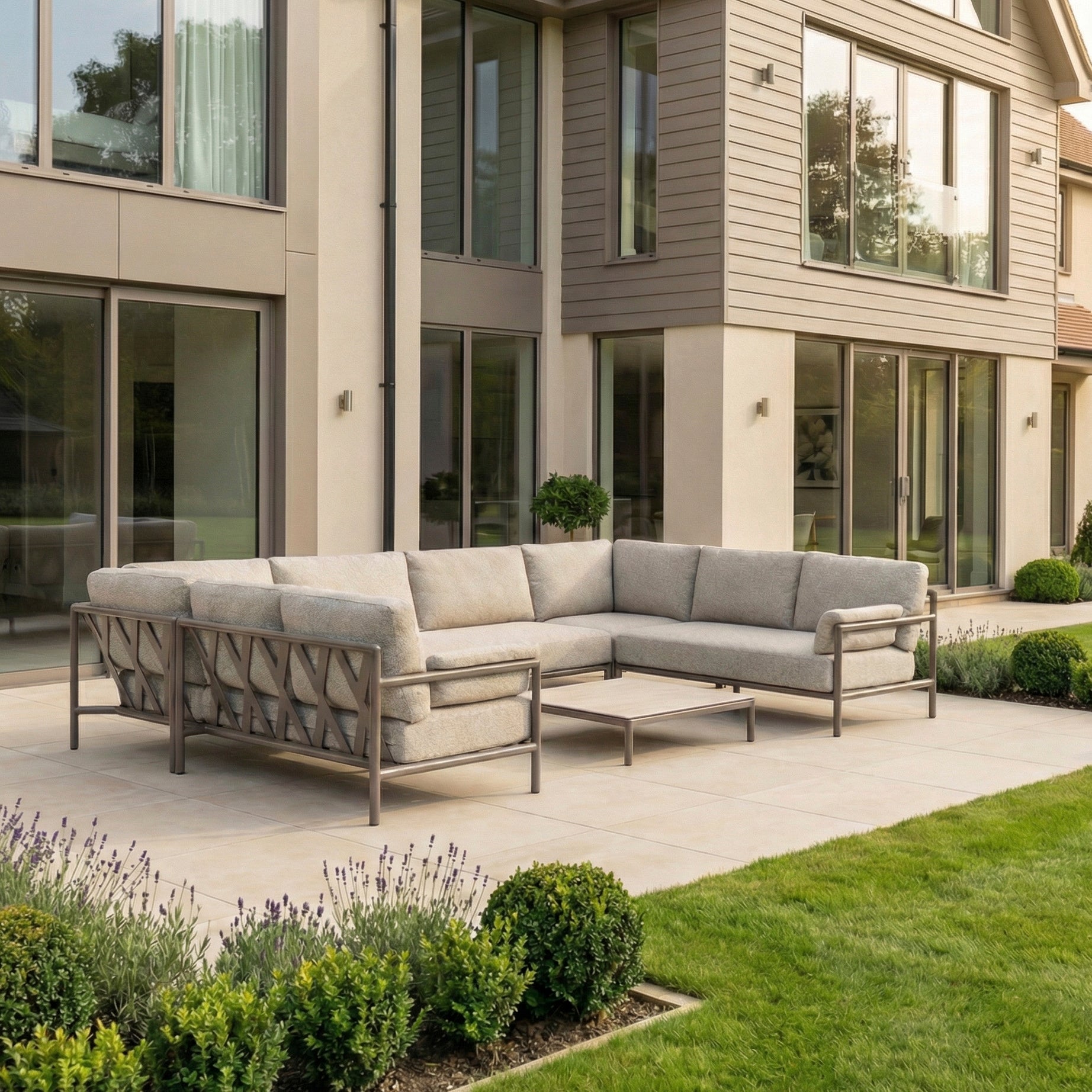 The Sorelli U Shape Corner Sofa Set in Oatmeal with boucle cushions and a small table is shown on a patio, in front of a modern house with large windows and a garden.