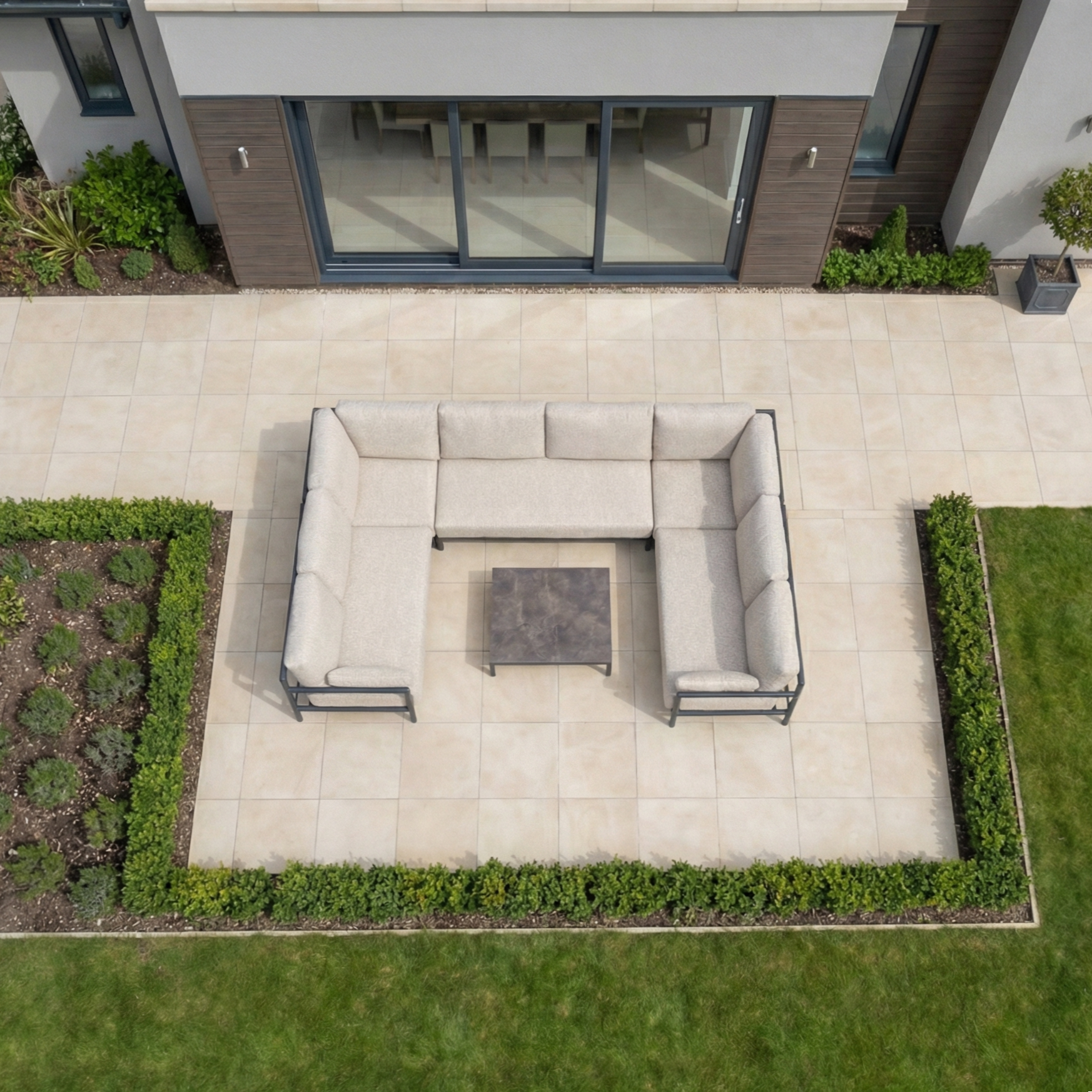 Aerial view of a patio with the Sorelli U Shape Corner Sofa Set in Truffle and a square coffee table, featuring weather-resistant cushions—ideal for outdoor entertaining amid lush grass and greenery.