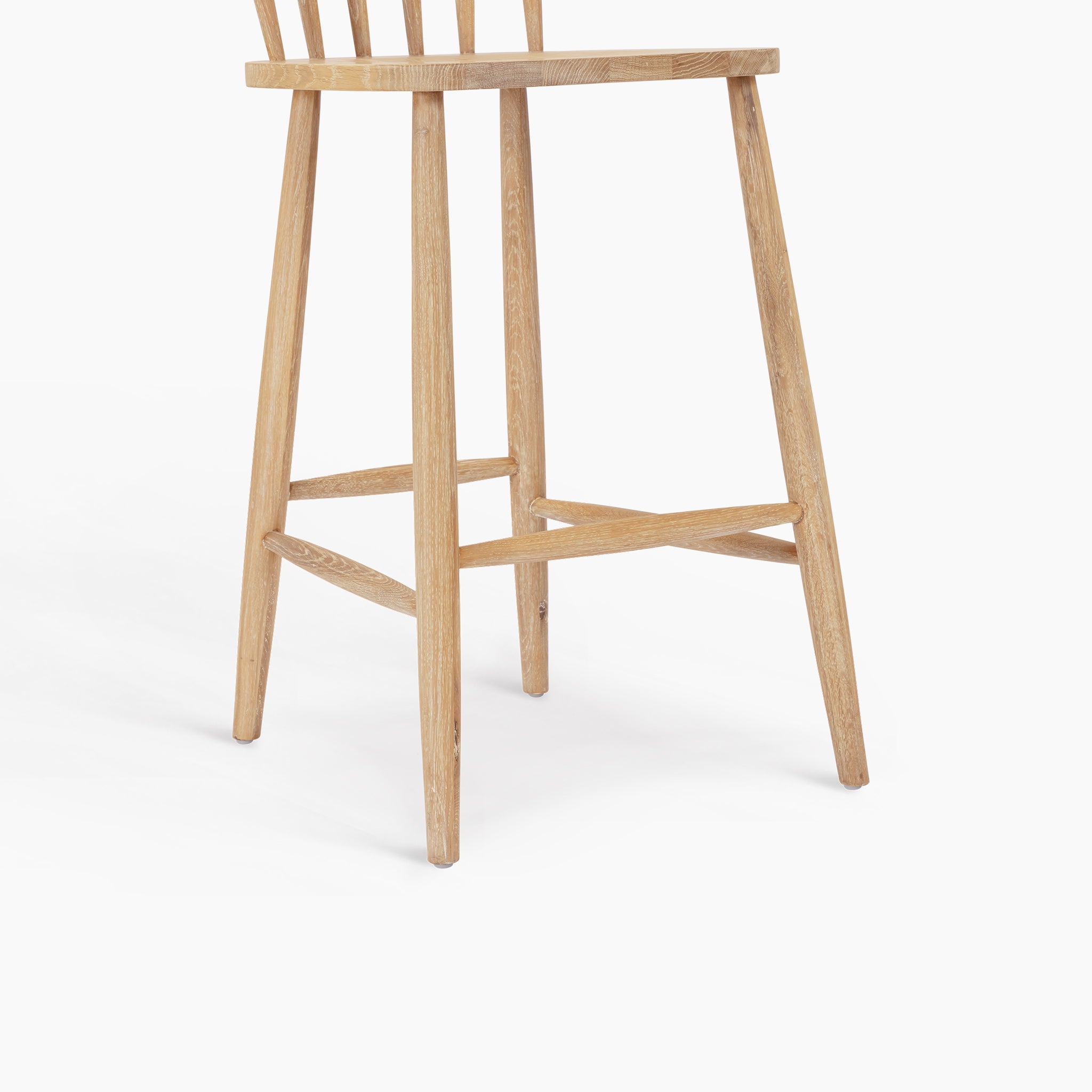 The Burford Spindleback Bar Stool in Natural Oak features angled legs and a simple, minimalist design, shown against a white background.