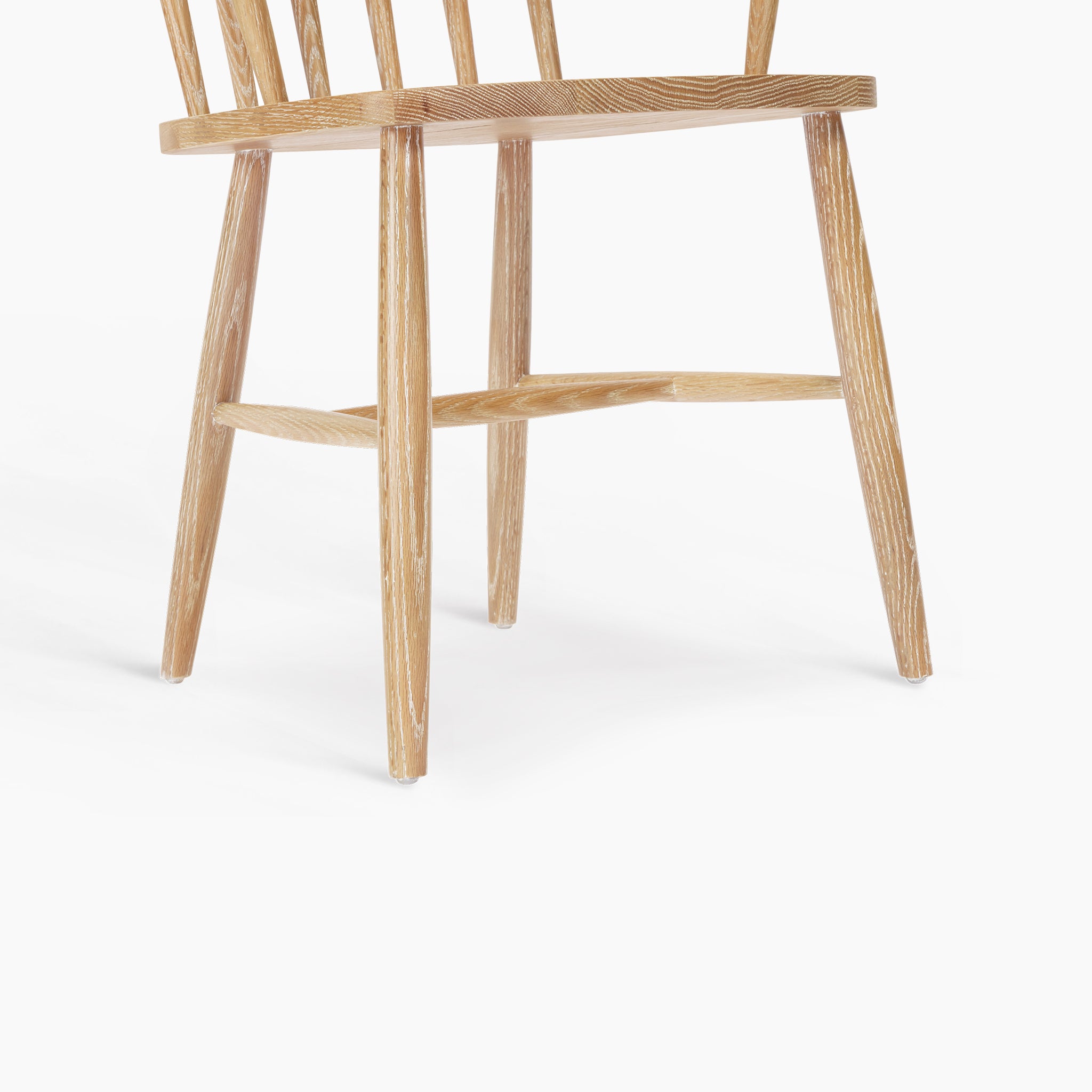 The Burford Spindleback Dining Chair with Armrest in Natural Oak features a spindle backrest and tapered legs, shown against a white background.