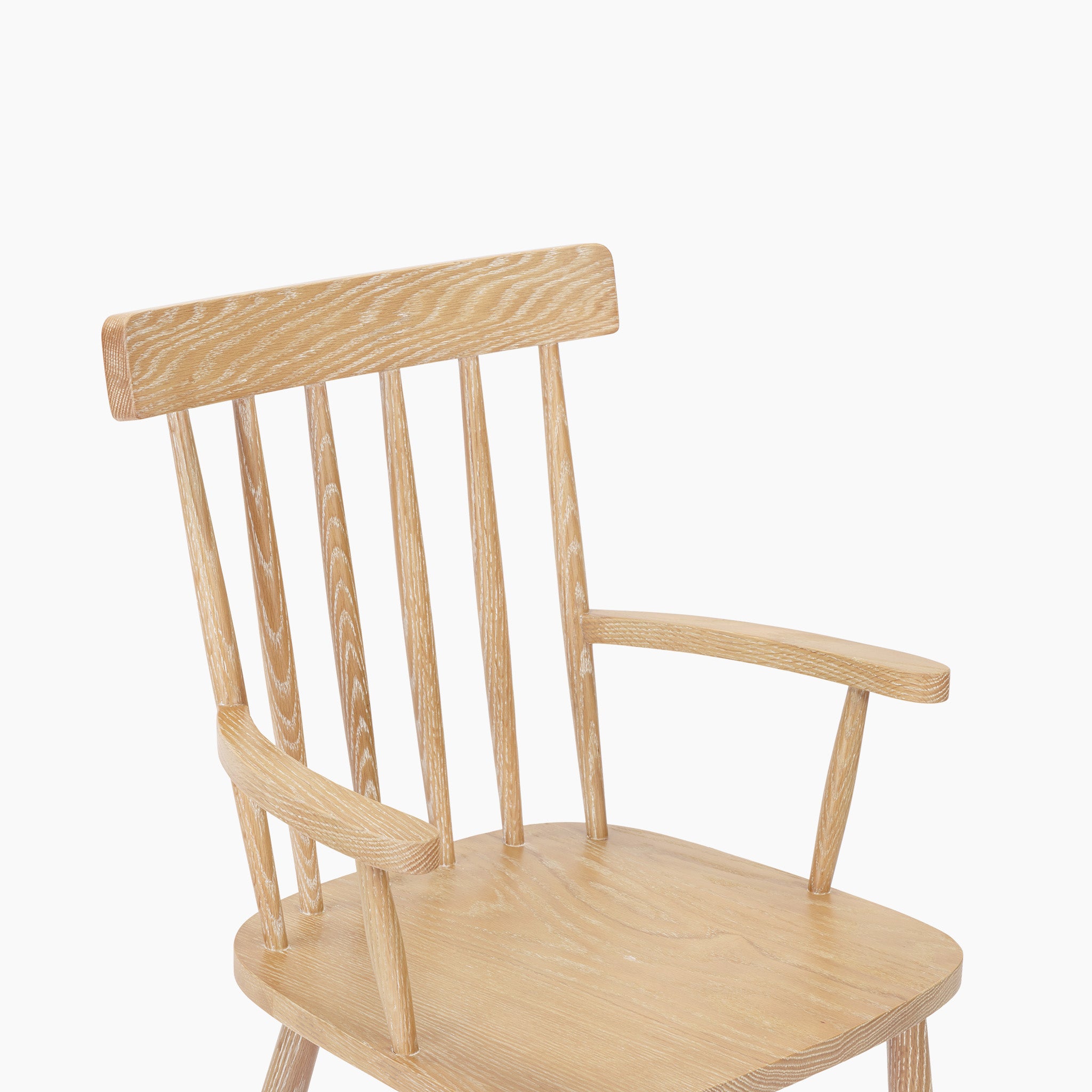The Burford Spindleback Dining Chair with Armrest in Natural Oak features vertical backrest slats and armrests, displayed against a white background.