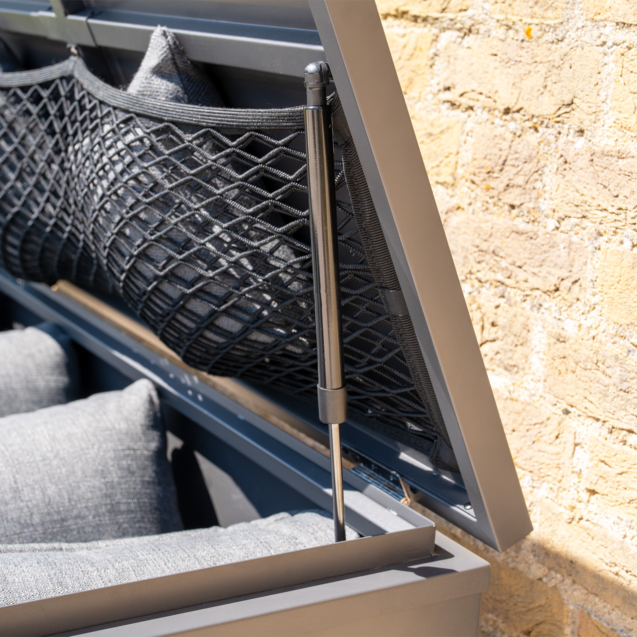 Close-up of the Large Steel Storage Box in Grey, showcasing an outdoor storage net pocket and gas strut hinge, safely storing gray cushions inside with a secure, watertight seal.