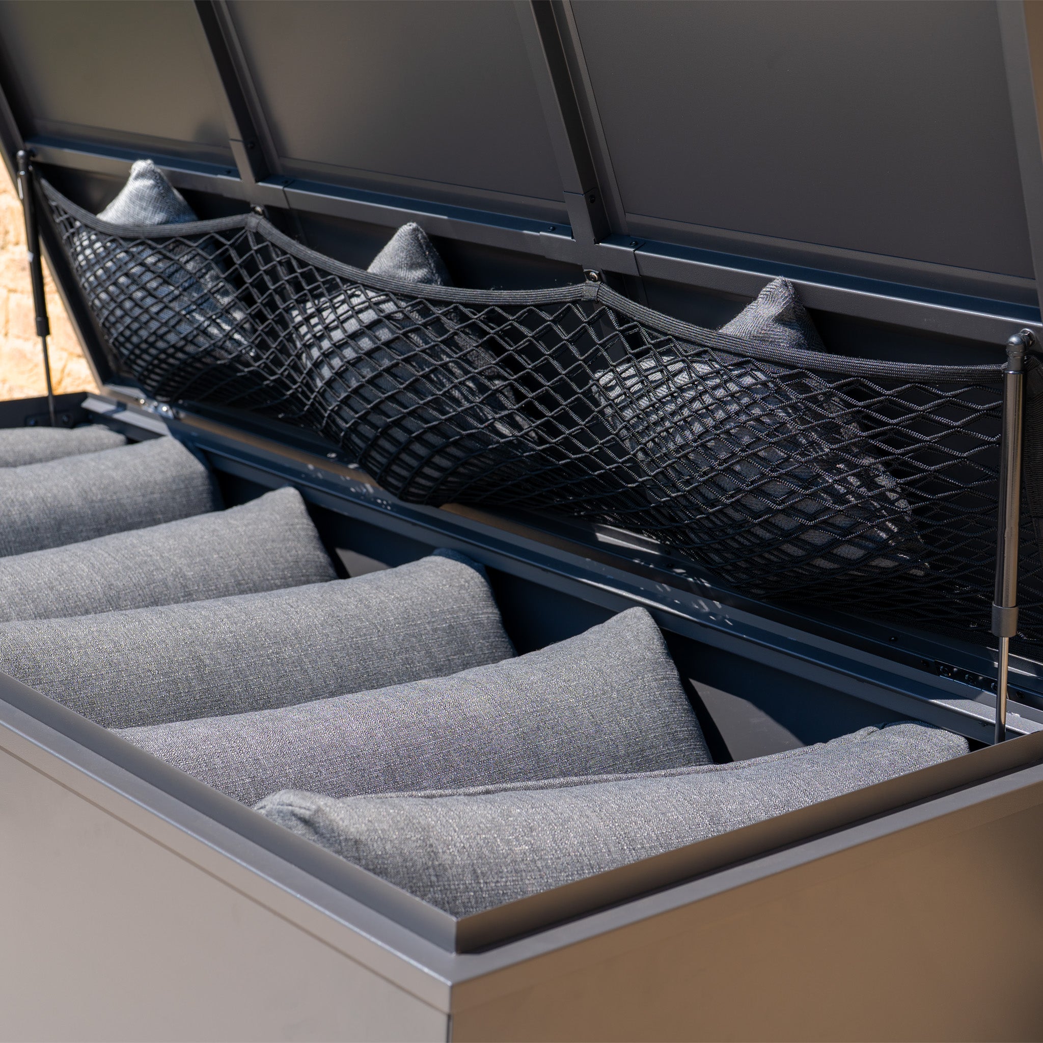 The Small Steel Storage Box in Grey features gray cushions neatly stored inside and extra space in the mesh lid pocket—an ideal waterproof garden storage solution.