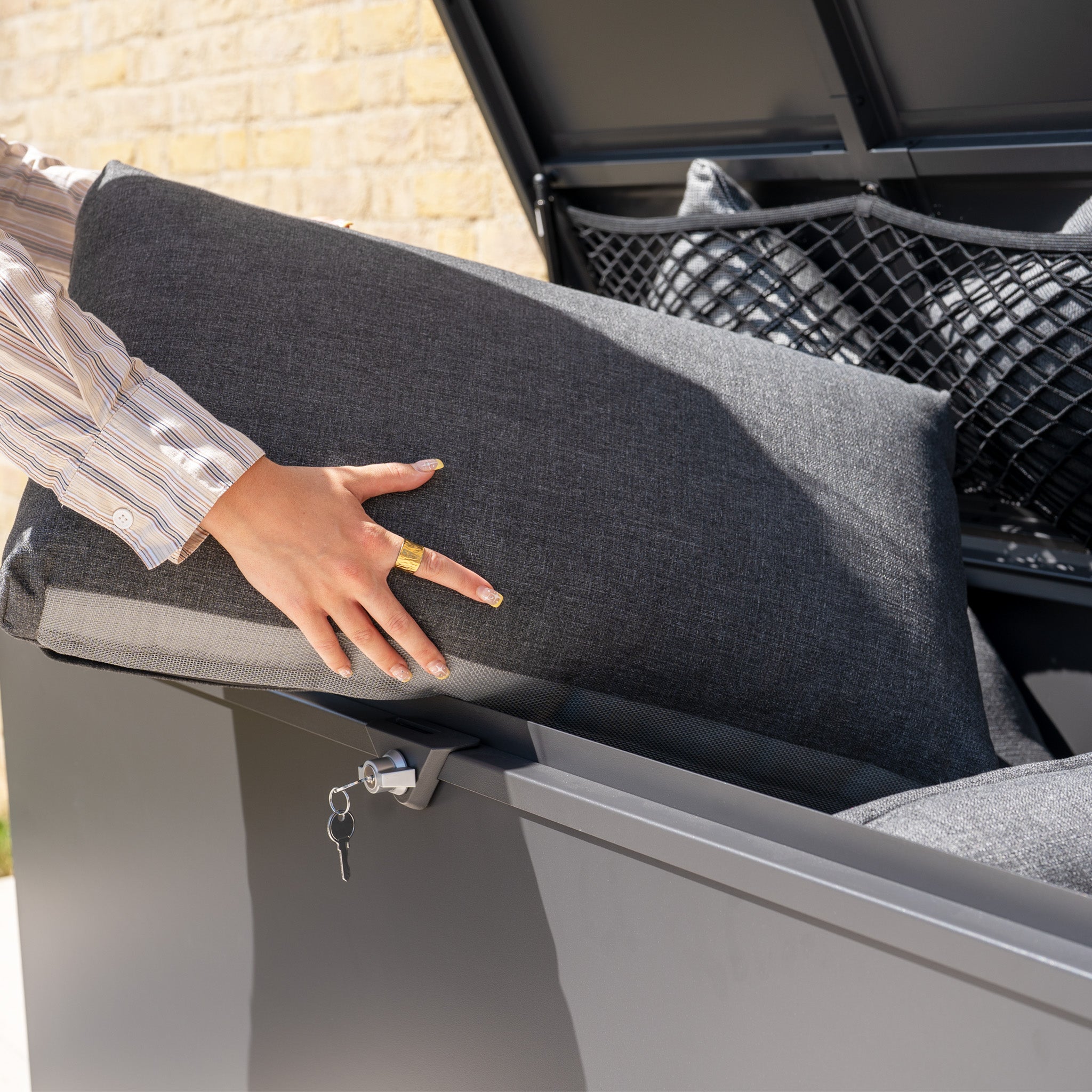 A person places a gray cushion into the Small Steel Storage Box in Grey and secures it by locking the box.