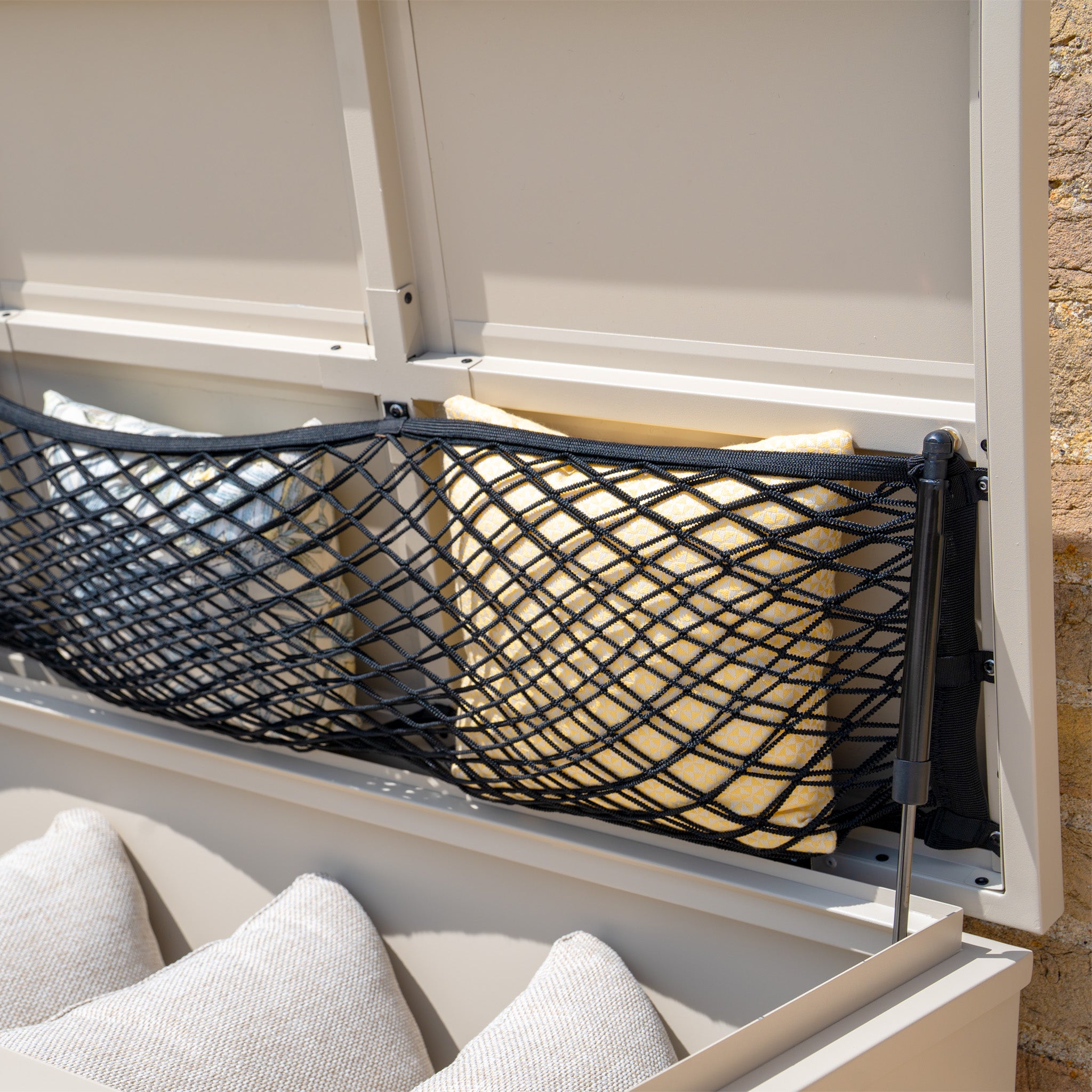 Close-up of the Small Steel Storage Box in Latte, featuring a watertight design with a black net inside the lid holding yellow and gray pillows—ideal for stylish outdoor storage or as a compact Small Storage Box solution.